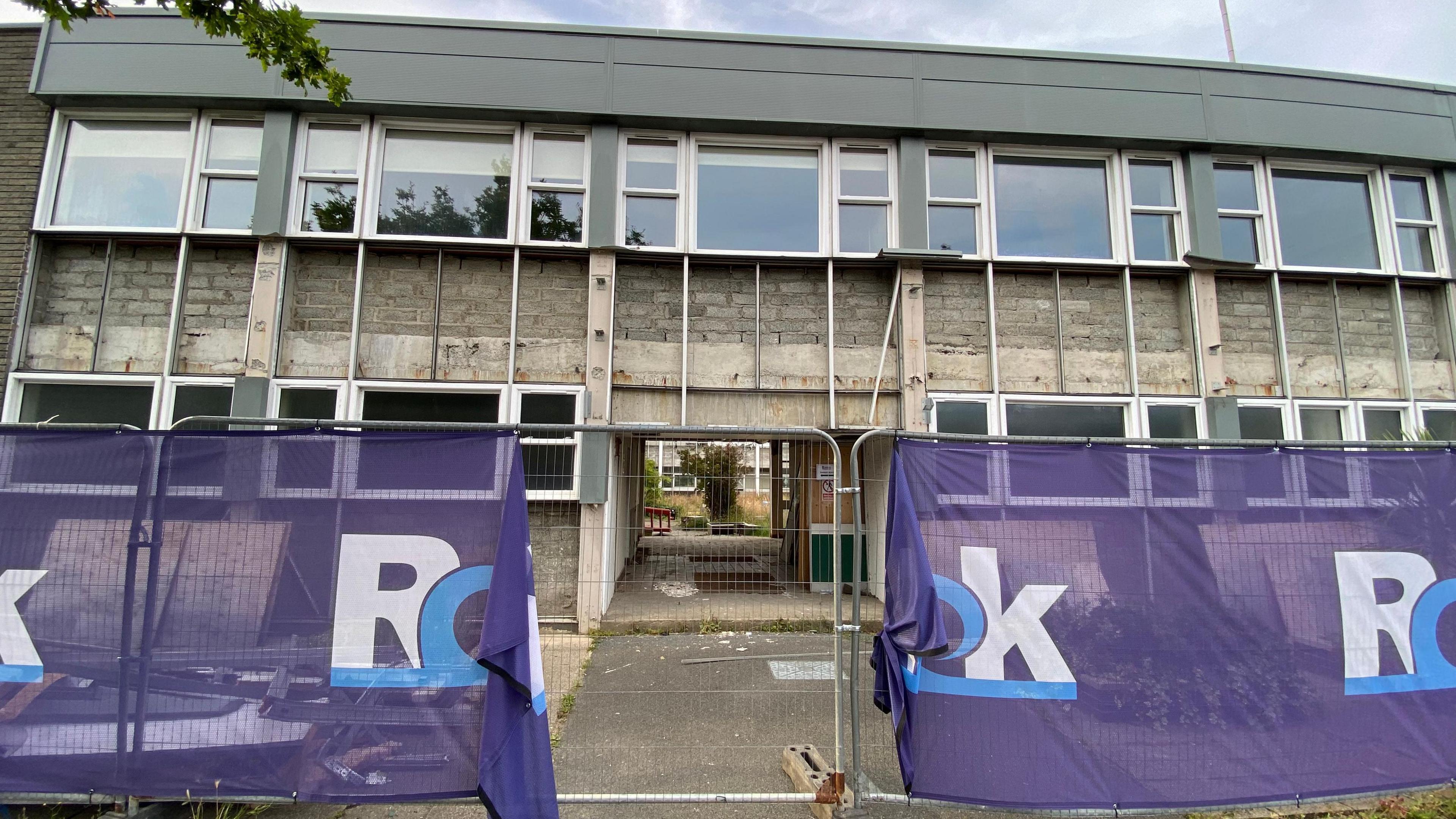 A protection fence is erected around a low rise college building before demolition and rebuilding. 