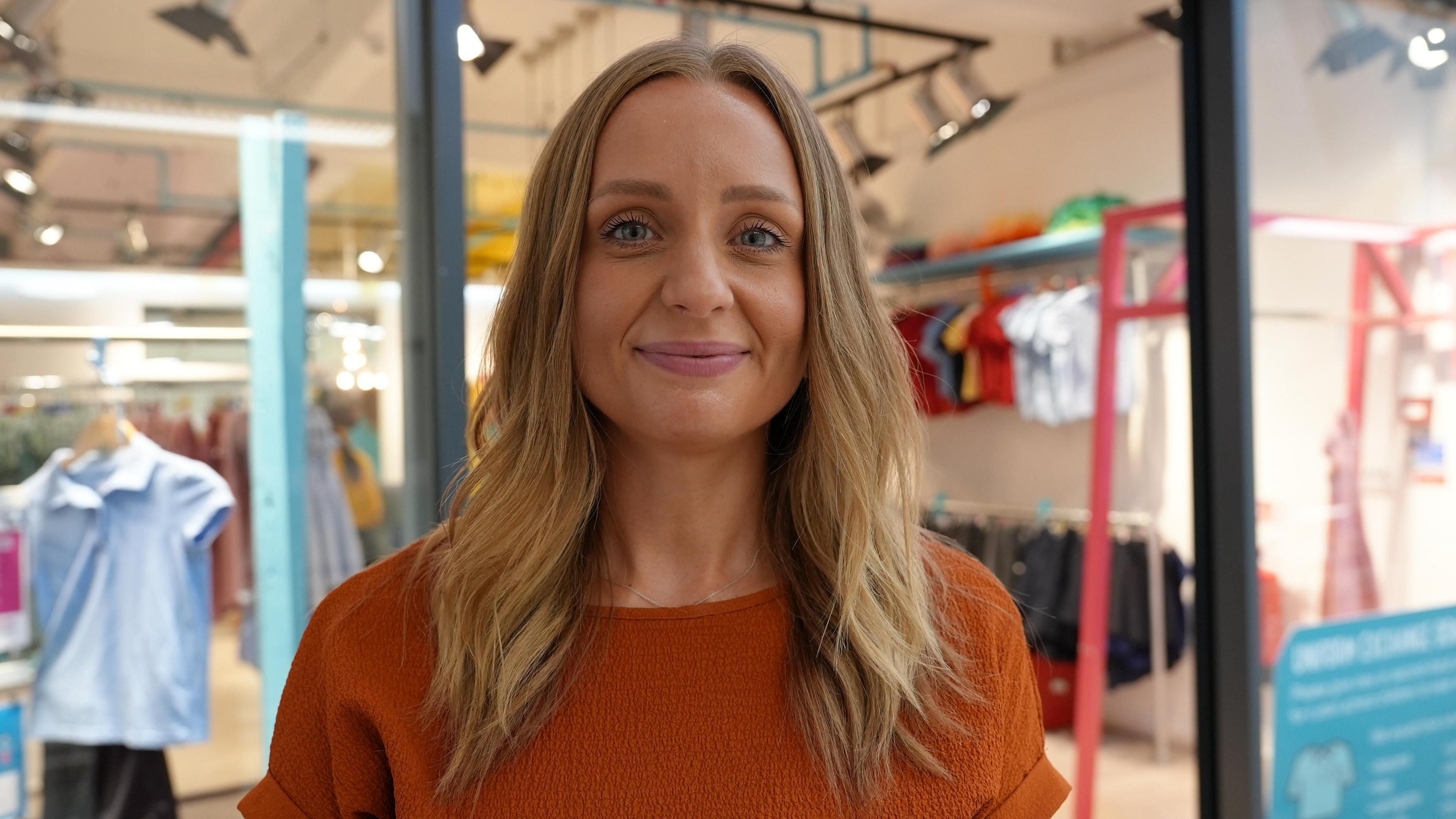 Kerri Porthouse wearing orange top and smiling with the uniform exchange behind her out of focus