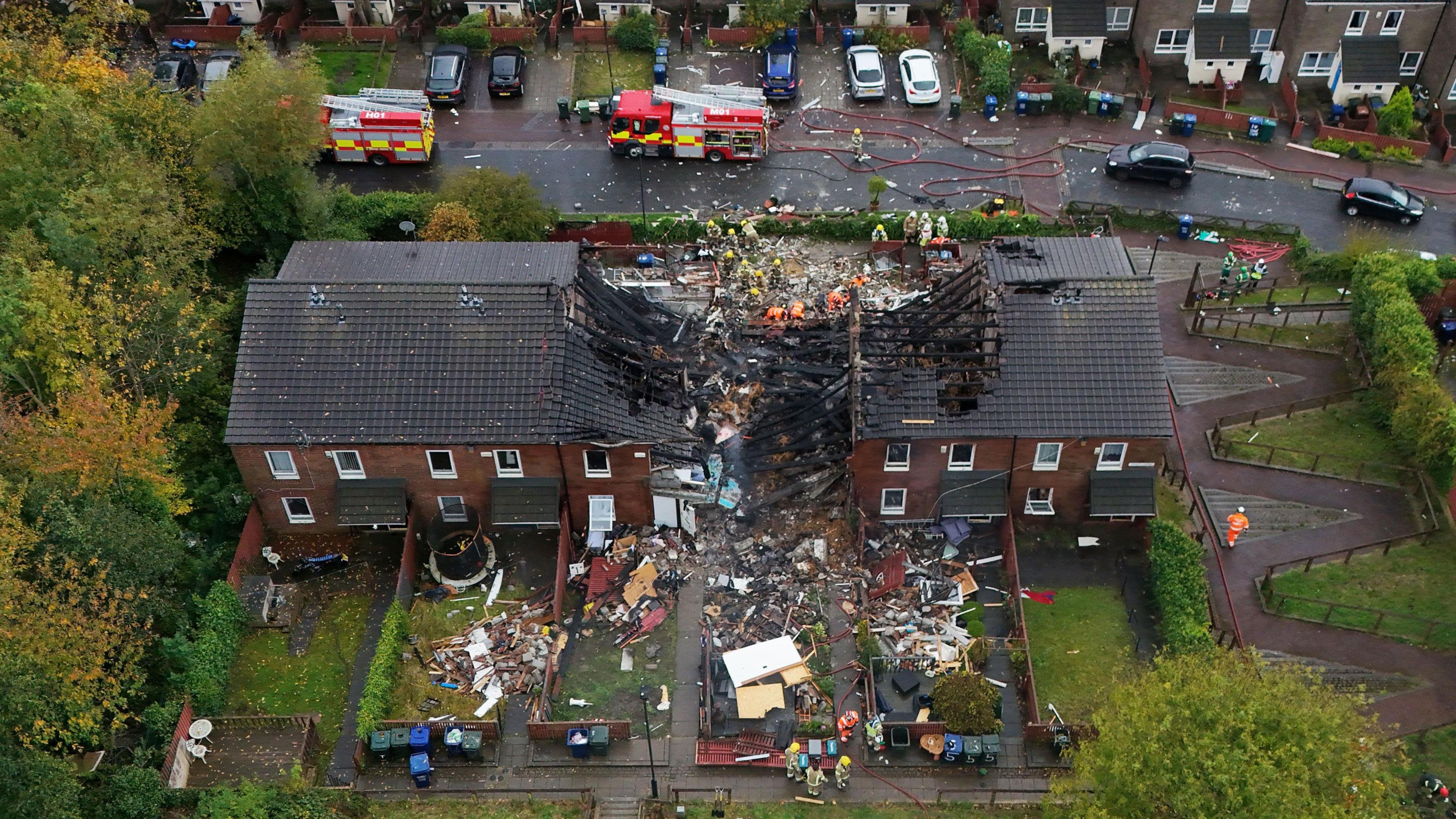 The explosion site. The middle of the terraced block is destroyed. Debris is scattered on the ground.