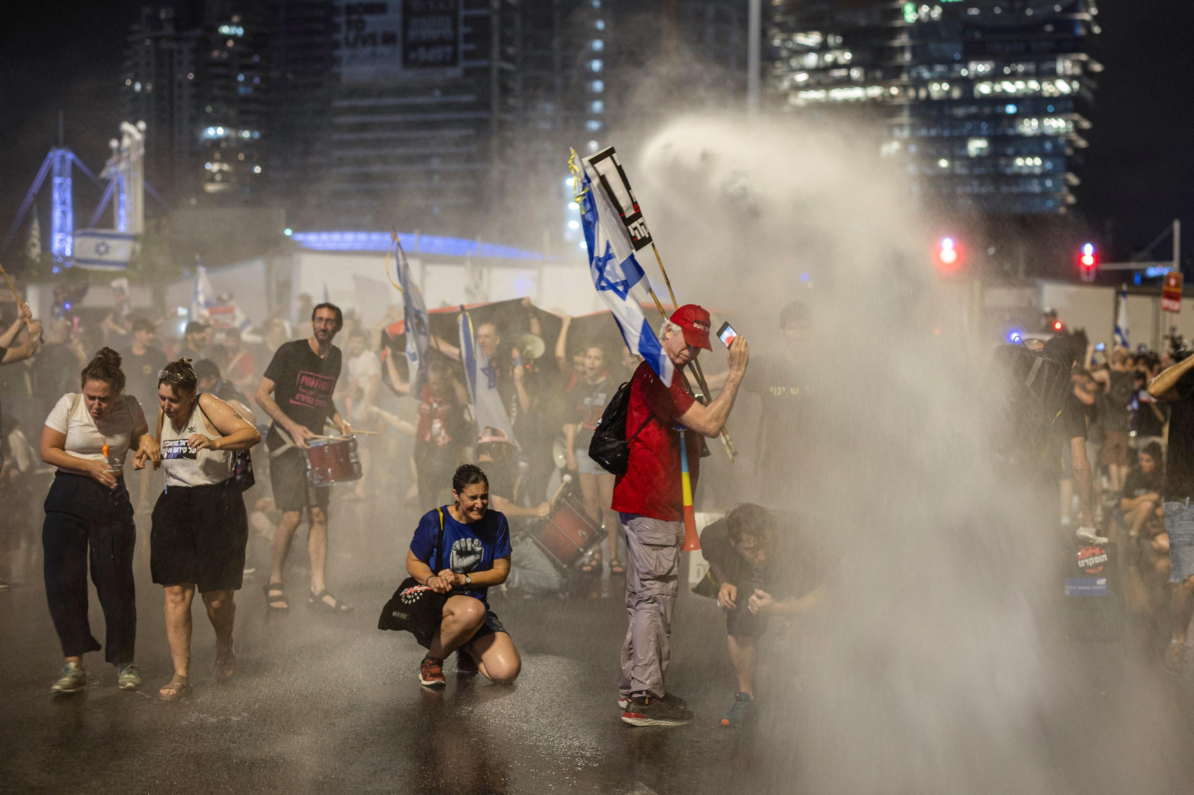 Demonstrators take cover from the Israeli police's water cannon, at a demonstration against Prime Minister Benjamin Netanyahu's government and a call for the release of hostages in Gaza, amid the Israel-Hamas conflict, in Tel Aviv