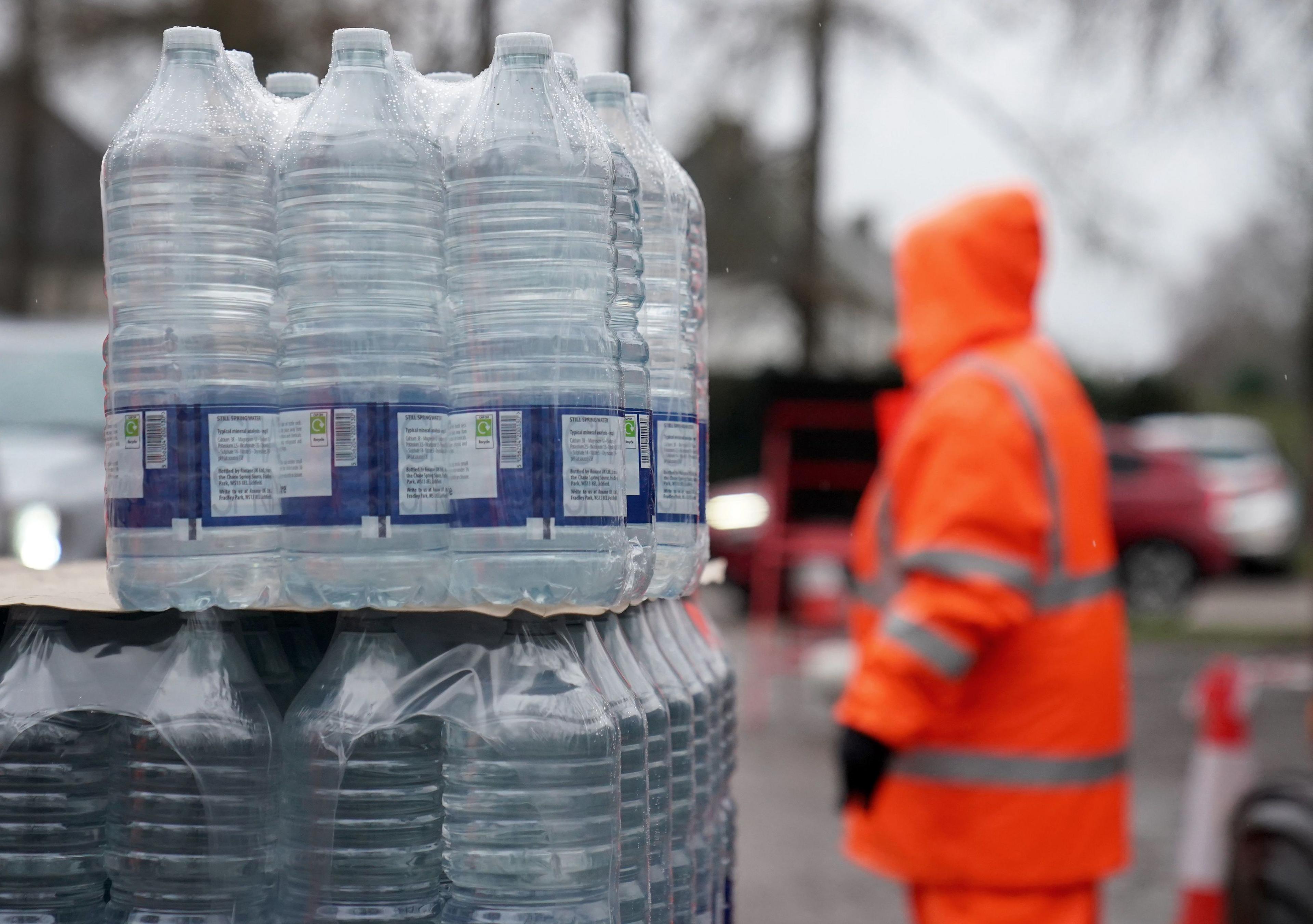A stack of bottled water in the foreground with a blurred worker in high vis orange in the background