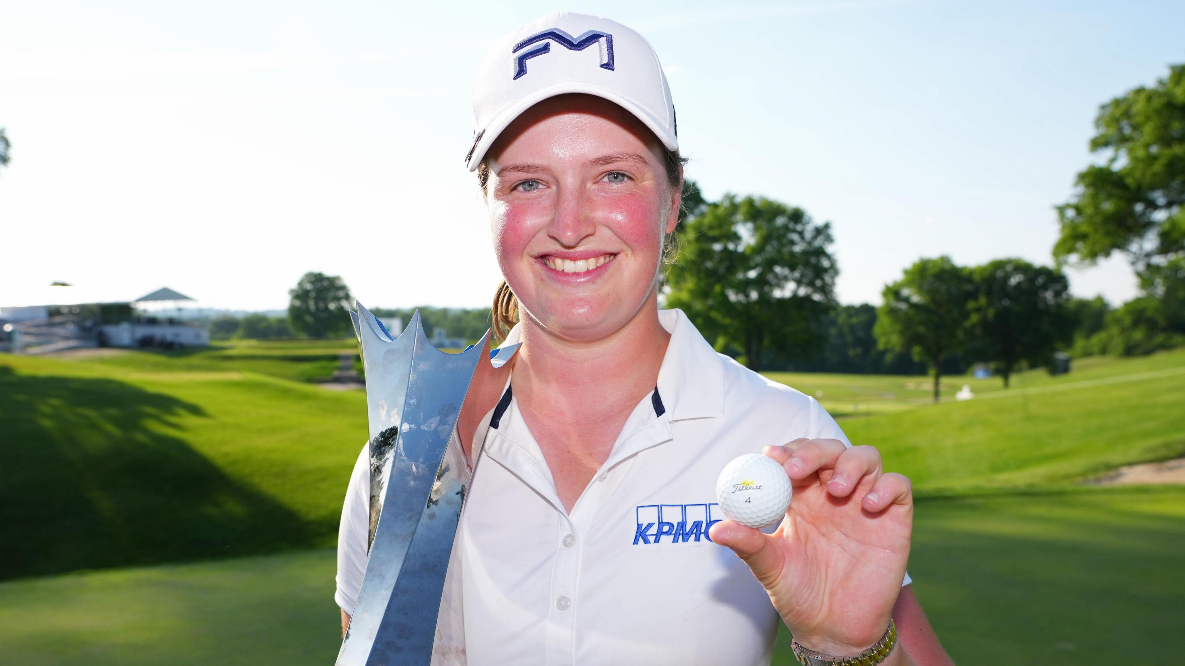 Lottie Woad smiling and holding a trophy and a golf ball