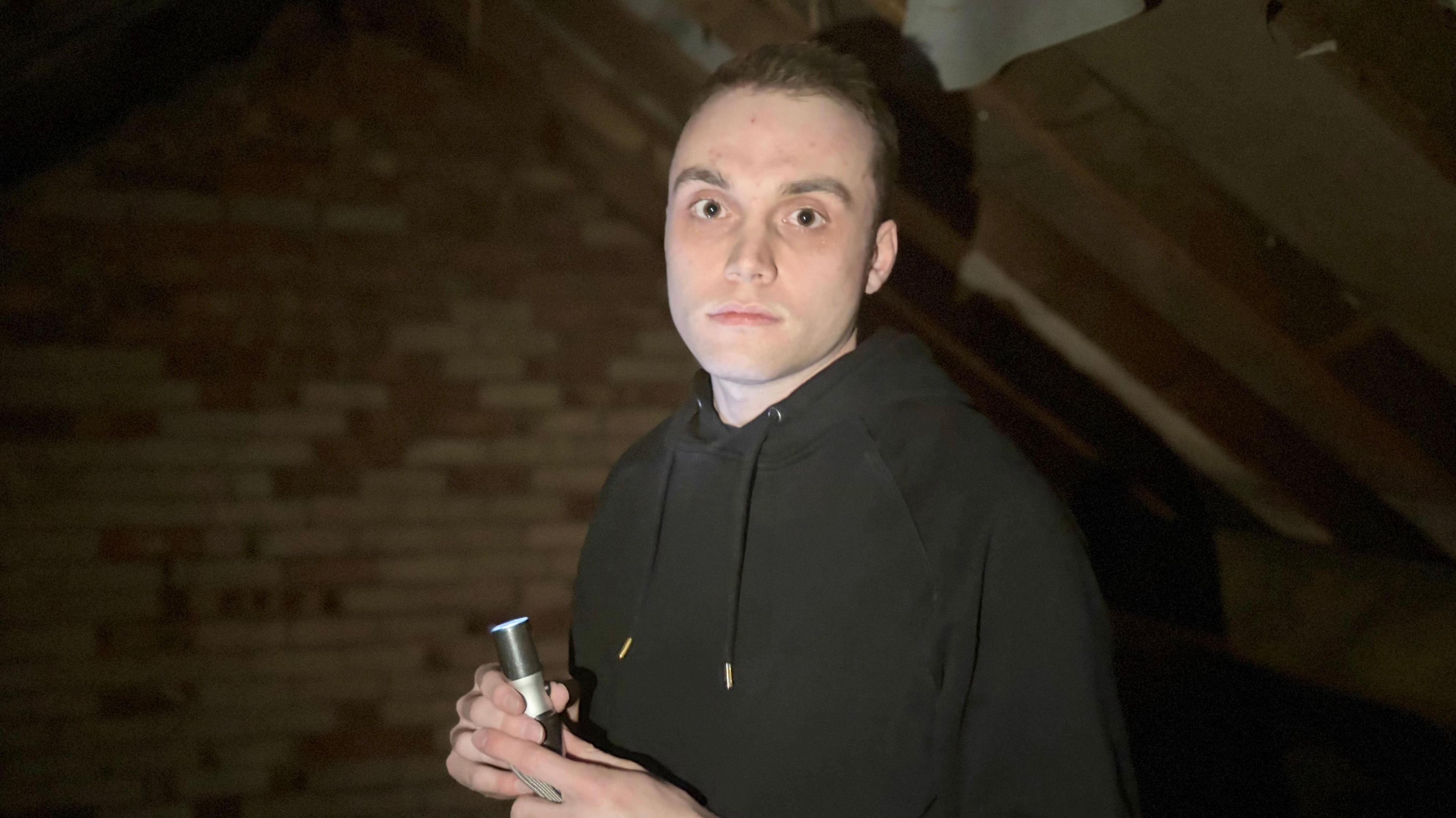 Joe Edgson is pictured inside a dark attic with a torch shining