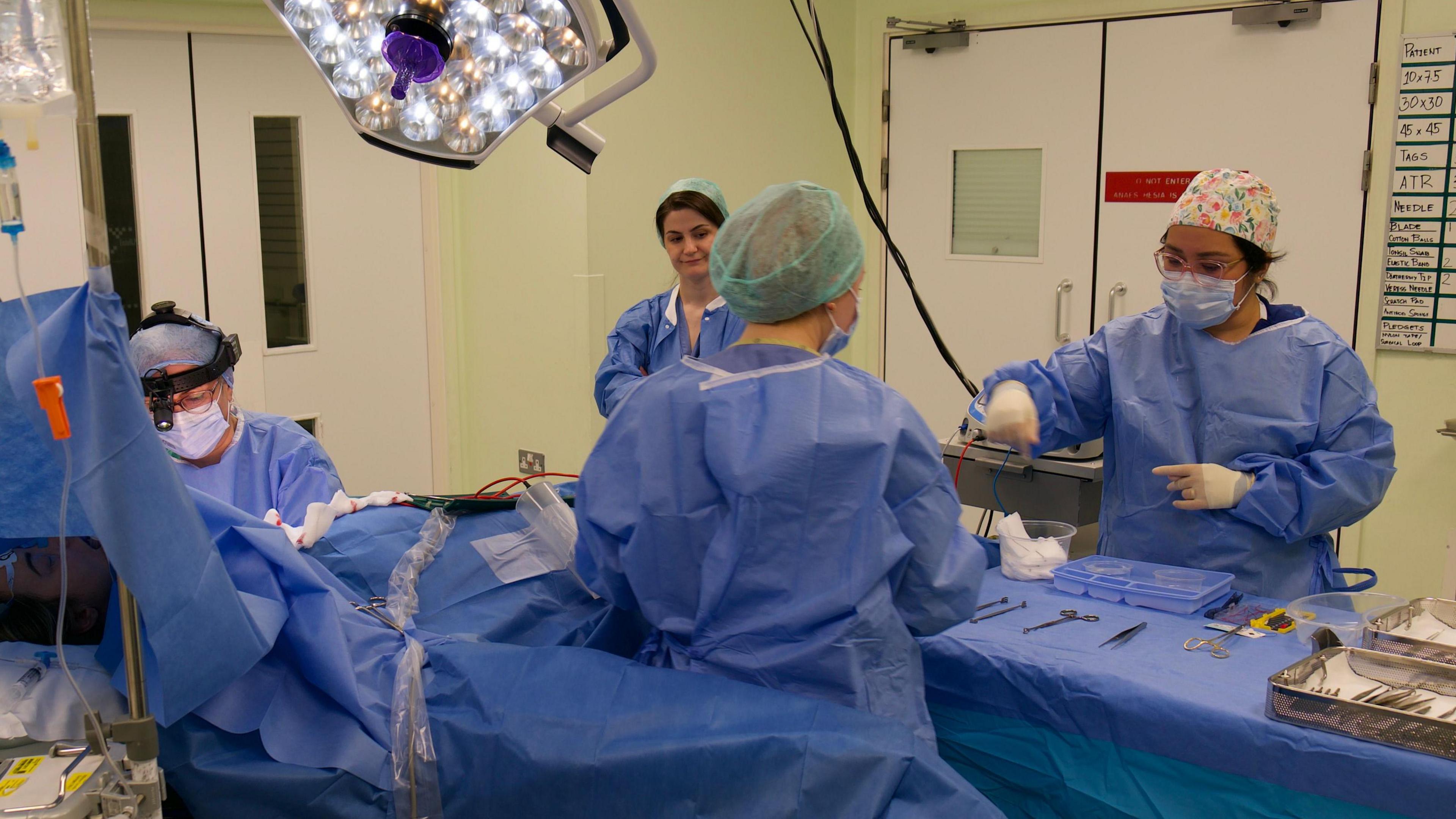 NHS doctors and nurses working in an operating theatre wearing scrubs and masks.