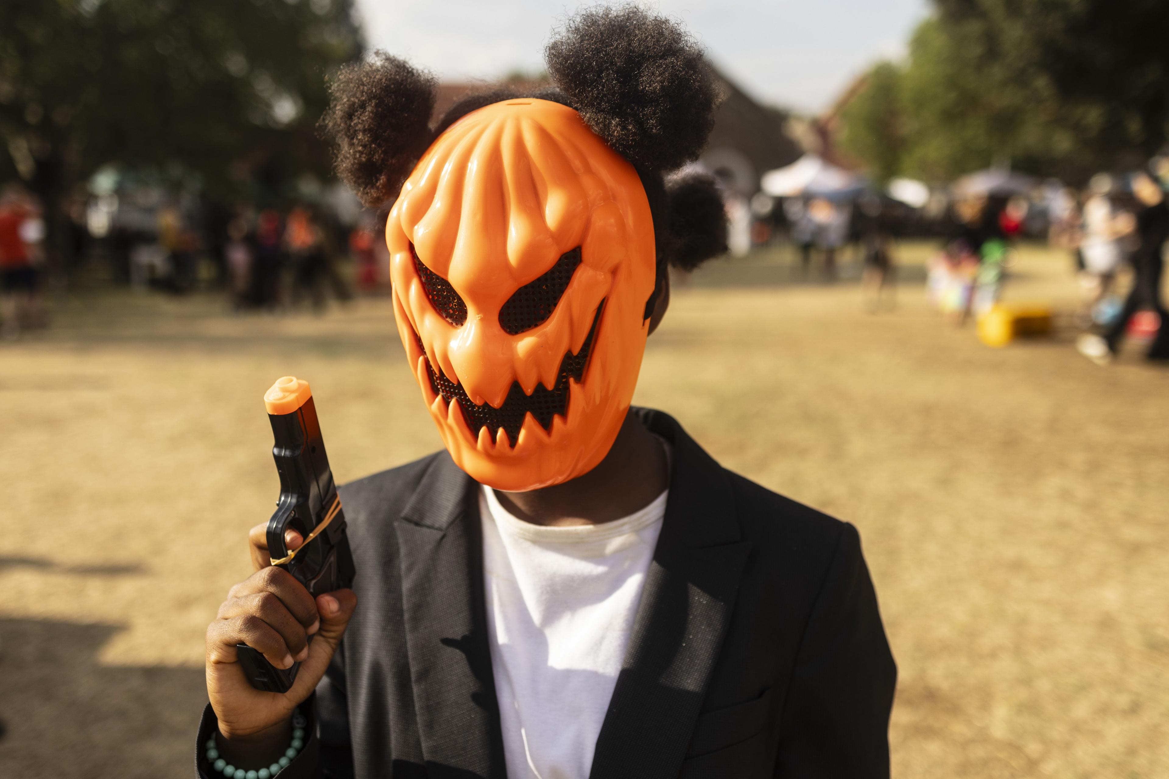 A young fancy dress contestant - wearing a pumpkin mask, toy gun, black blazer and afro puffs - waits to take part in in the best-dressed competition during the annual Halloween party at the George Hay Park. The event aims to raise funds to maintain and improve the neighborhood's green spaces.