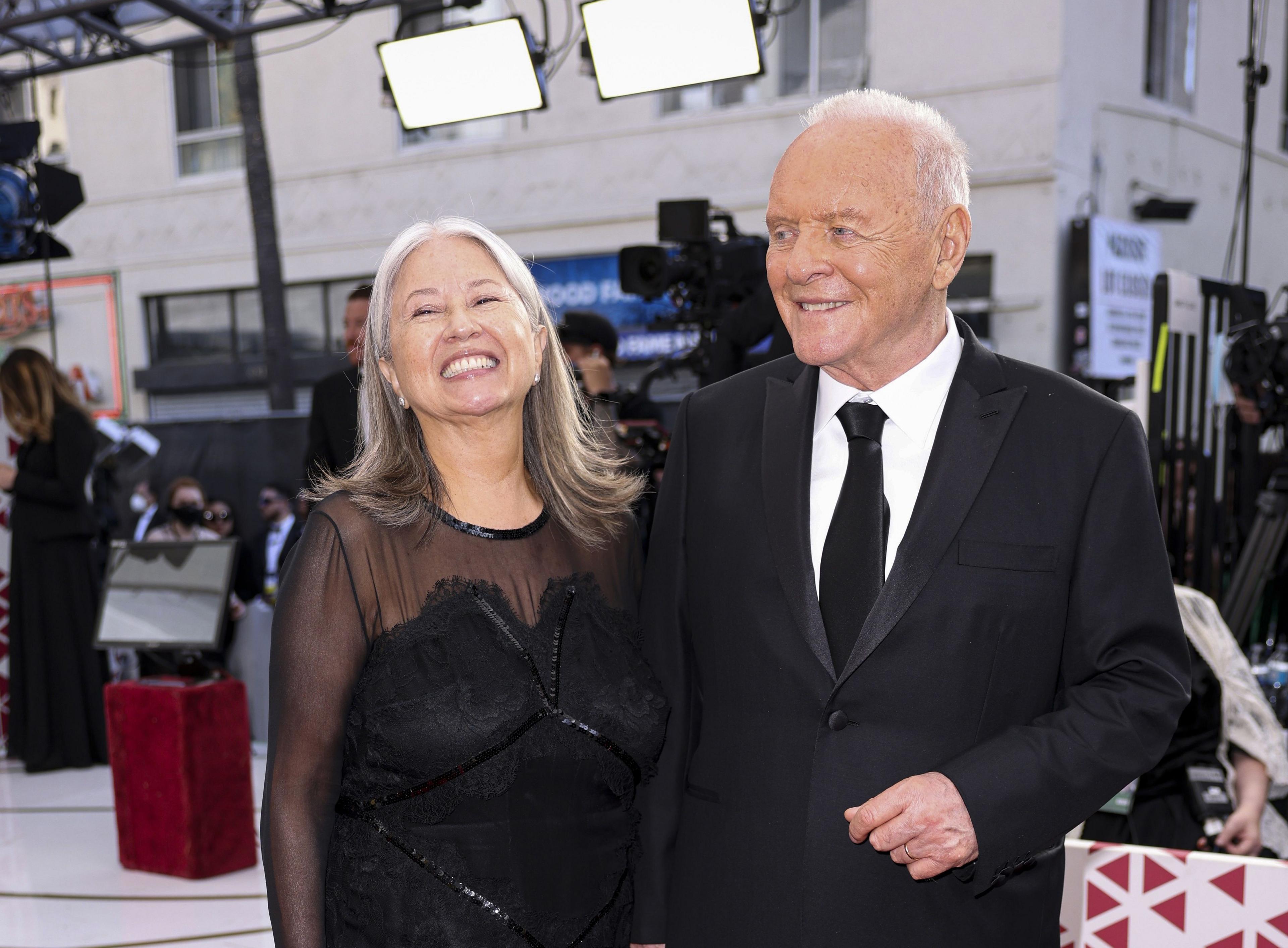 Stella on the left smiling in black chiffon and lace dress and Sir Anthony in black suit with white shirt