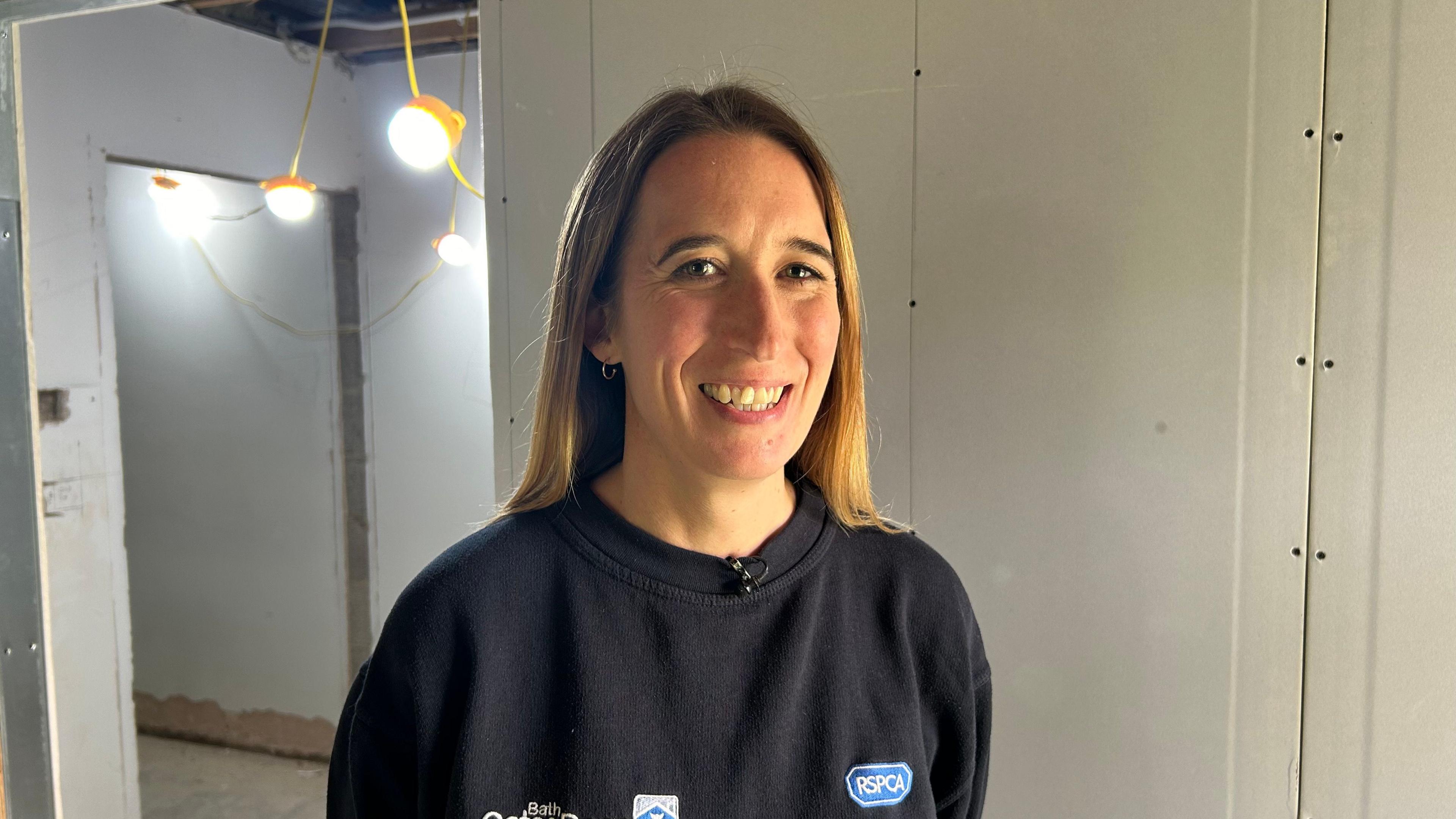 Photo of guest Rachel Jones, CEO of Bath Cats and Dogs Home. She is standing in the corridor of a refurbished building which is still under construction. She is wearing a blue t-shirt and has mid-length blonde hair 