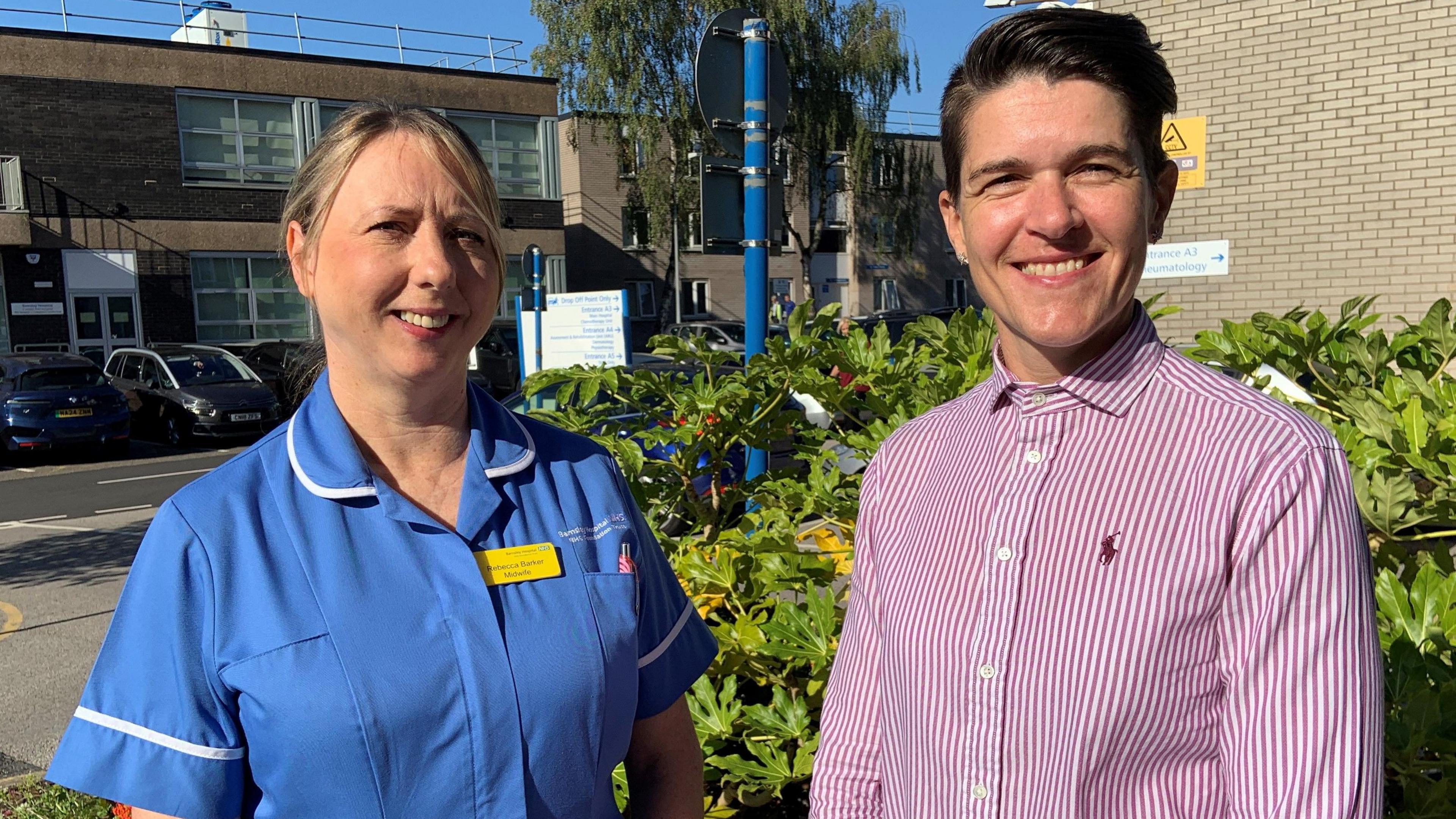 Midwife becky barker stands on the left in a blue uniform. She has her hair tied back. Kaye Mann has short dark hair and wears a red and white striped shirt. Both are smiling.