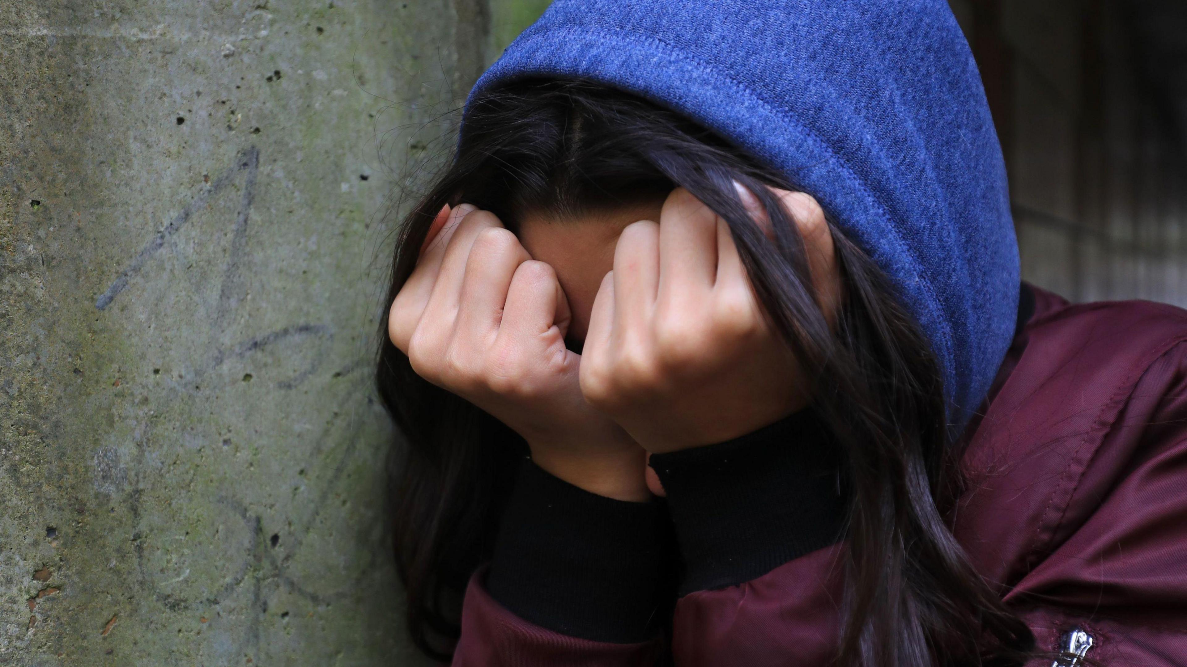 A stock image of a young girl holding her face in her hands.