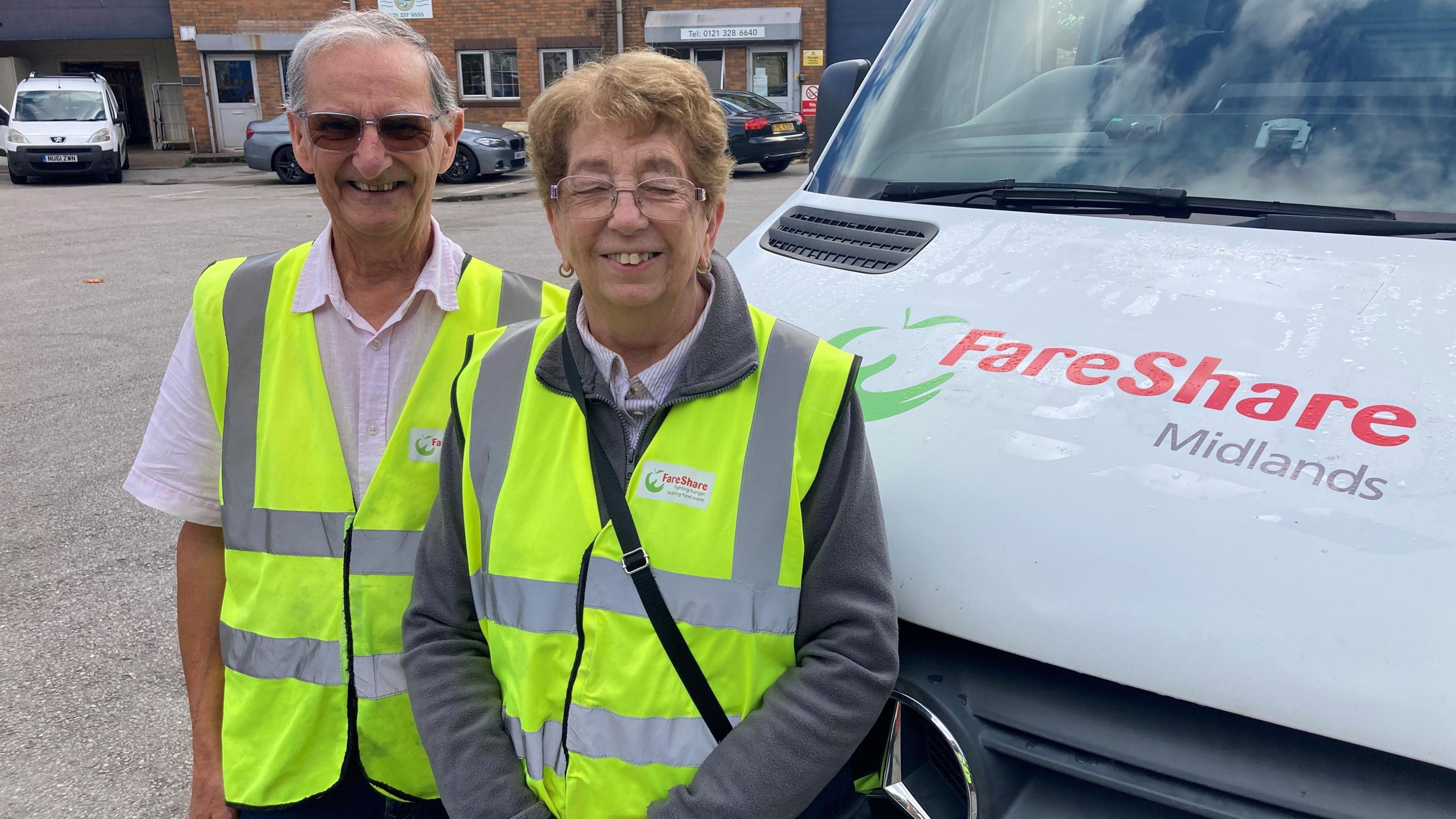 A man and woman in high-vis jackets standing in a warehouse carpark next to a Fareshare Midlands van