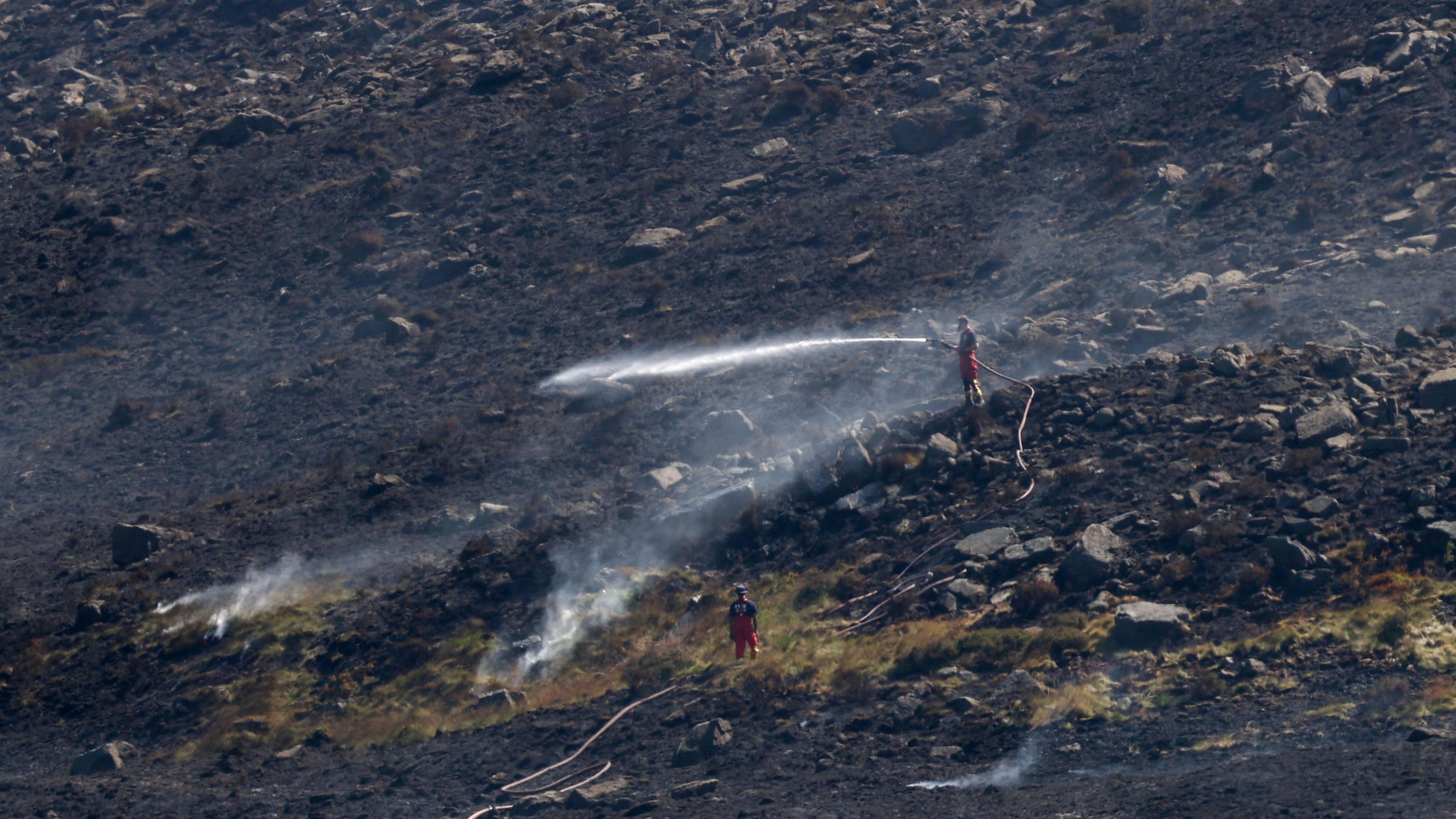 Firefighters on moor with hosepipes a lot of the land is black from burning