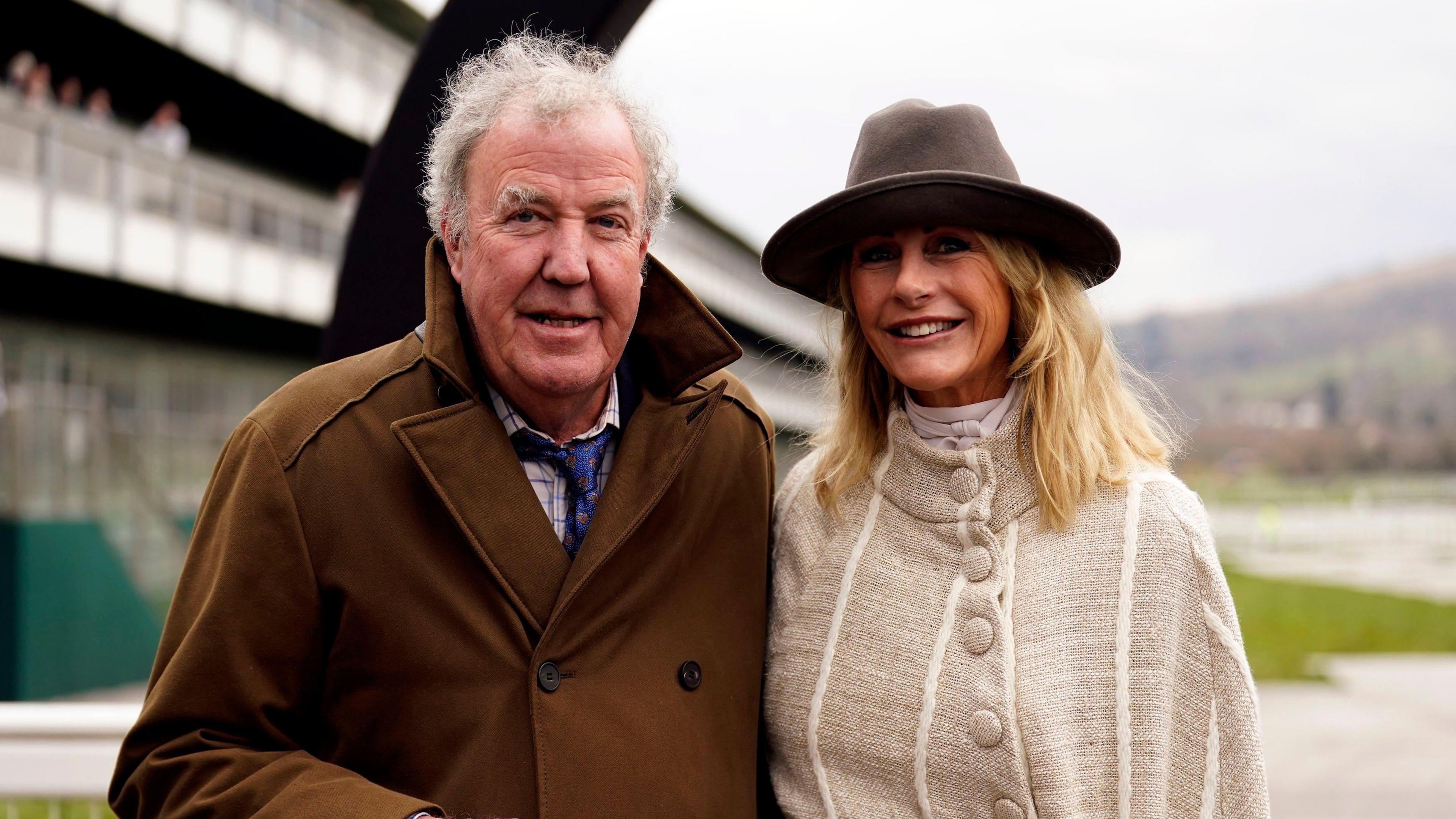 Jeremy Clarkson is on the right wearing a dark brown jacket, a white shirt and blue tie. He stands next to his girlfriend Lisa Hogan.