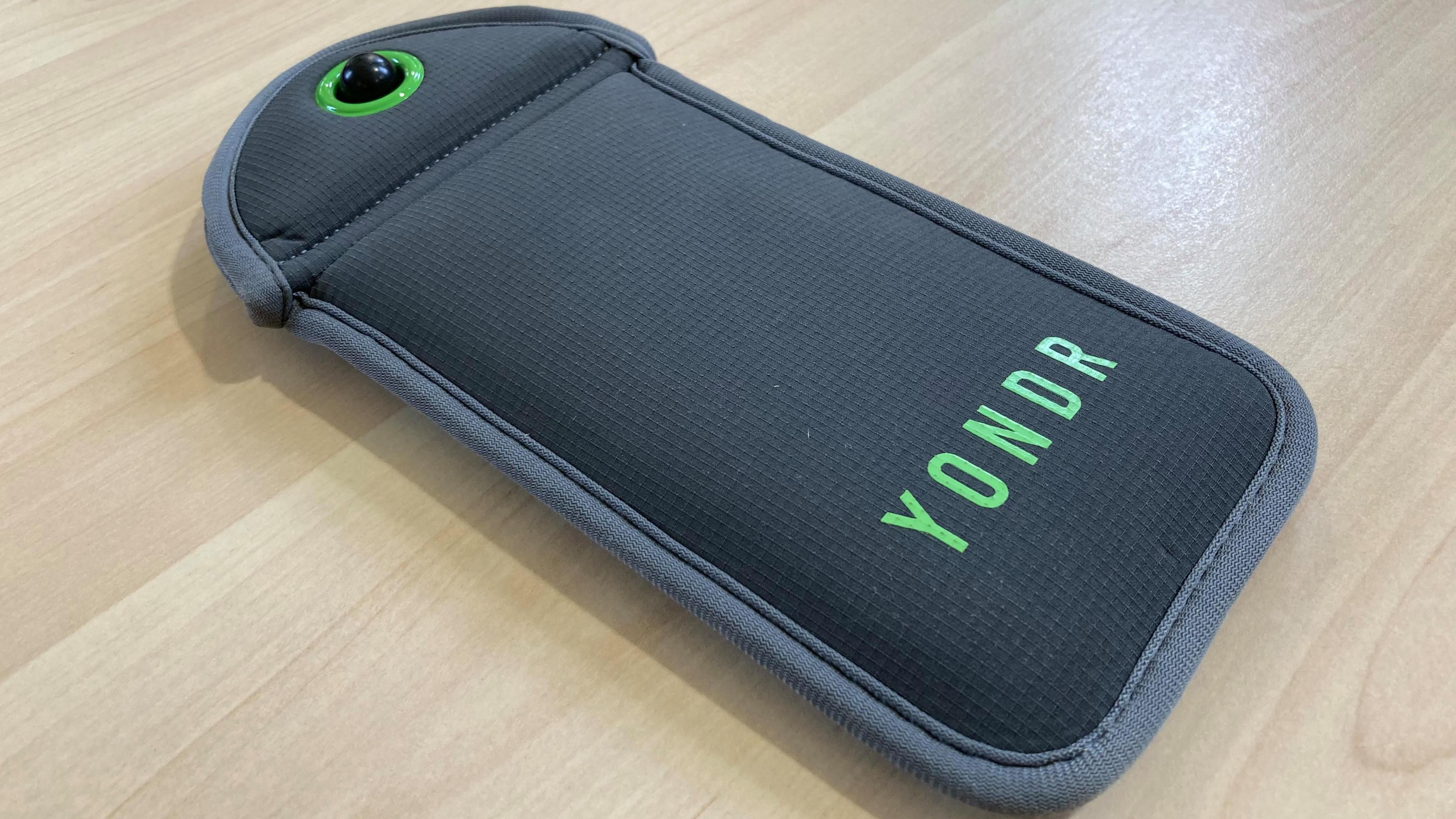 A grey rectangular pouch with the brand name Yondr in green on it. The top of the pouch has a locking device that looks like a black ball surrounded by a green circle.