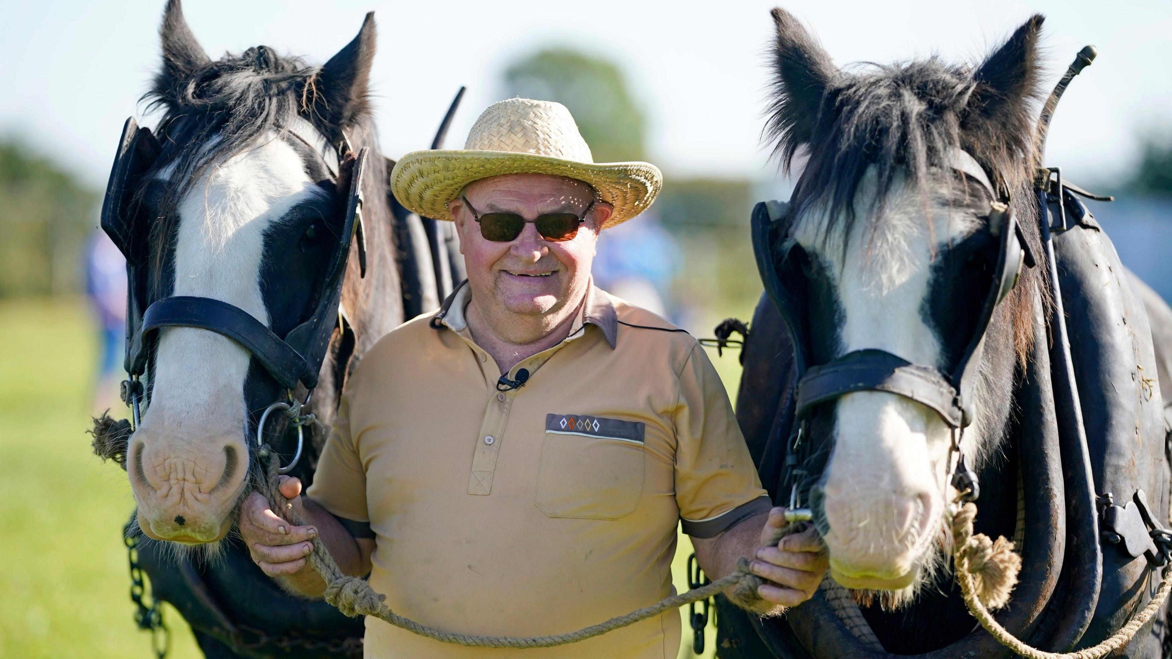 Gerry North from Offaly with horses Rooney (left) and Sunny at the National Ploughing Championships. He is wearing a dark yellow polo shirt and a straw hat and sunglasses. He is holding each horse by the bridle.