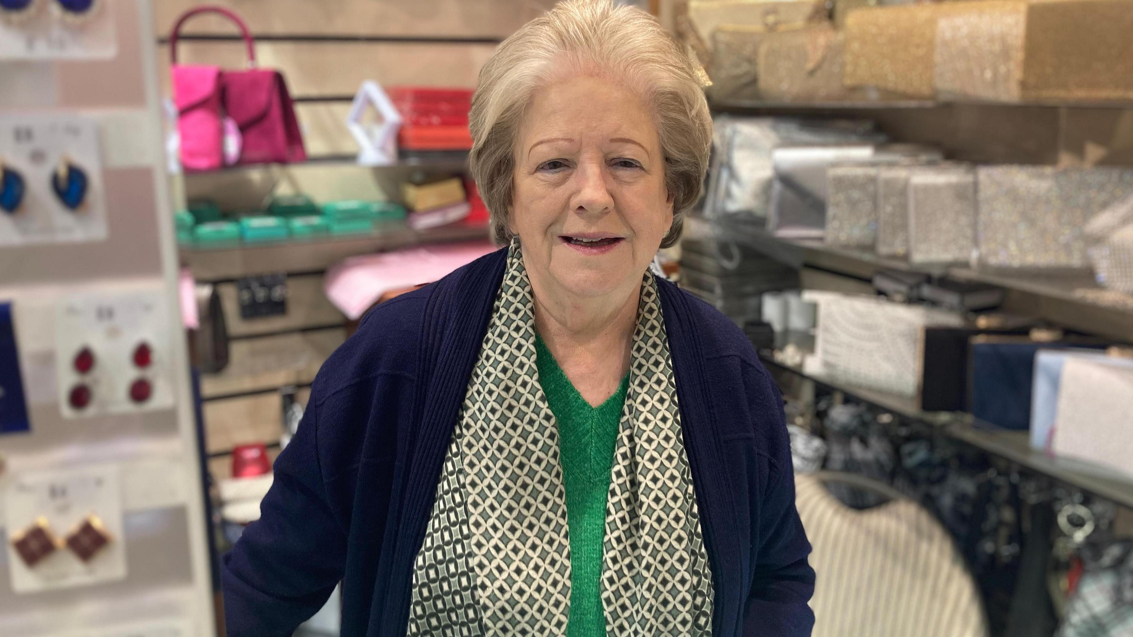 Eileen Lippa with blue jacket, green V-neck sweater and light green patterned scarf in a gift shop