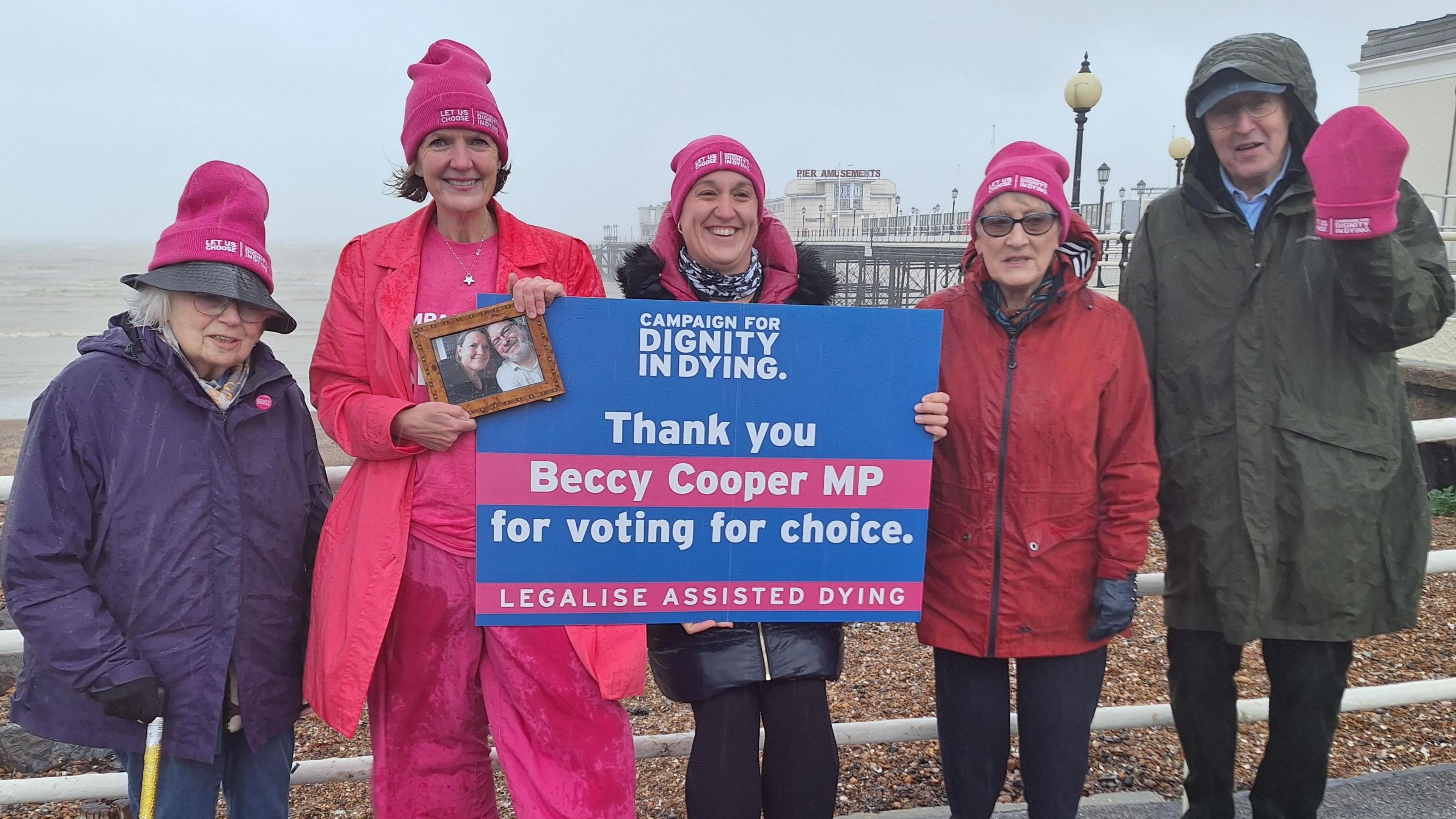 Five people standing on a promenade with a pier in the background. They are holding a sign that says "Thank you Beccy Cooper MP for voting for choice."