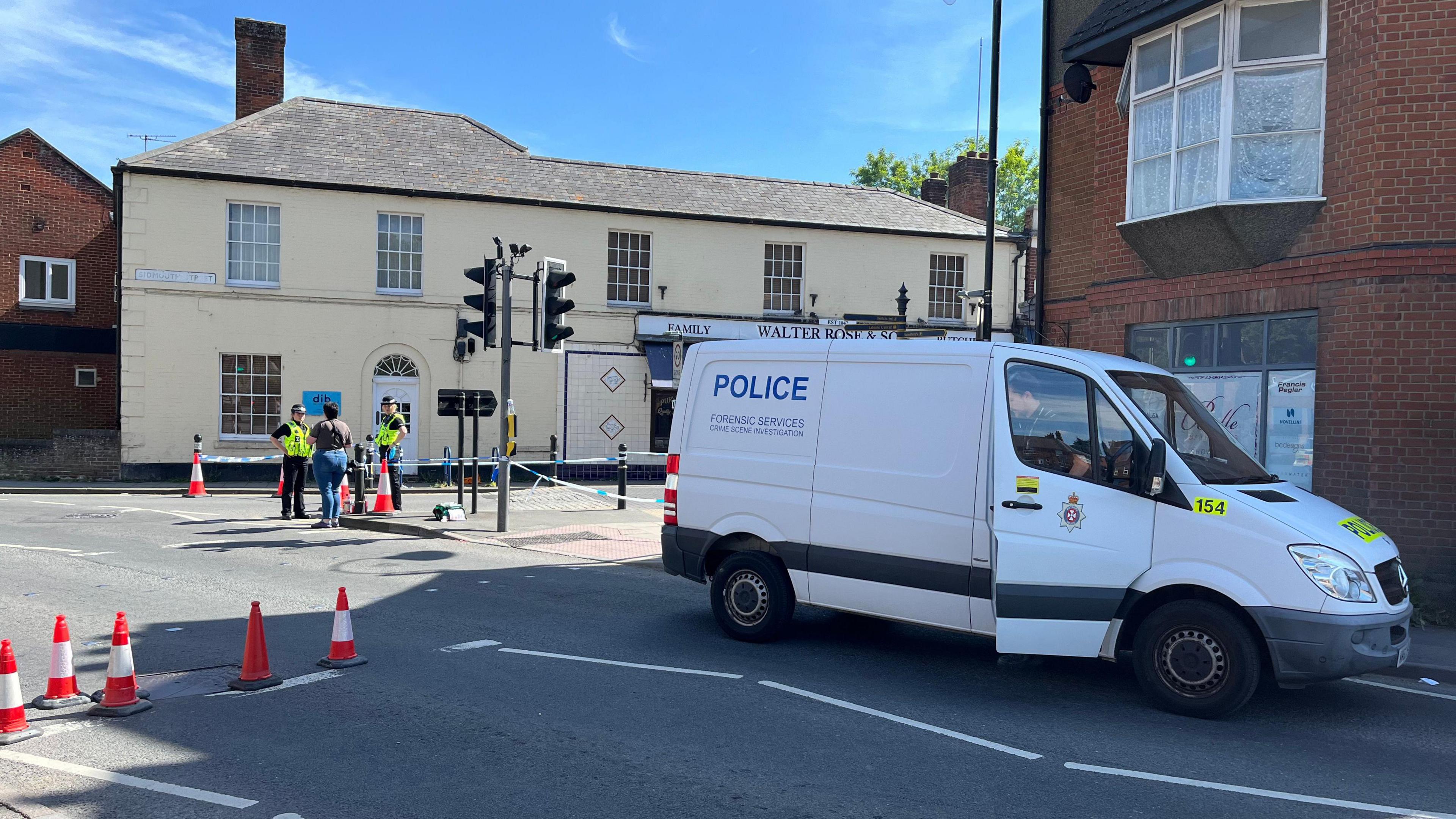 Police and police van at road near cordon with police tape.