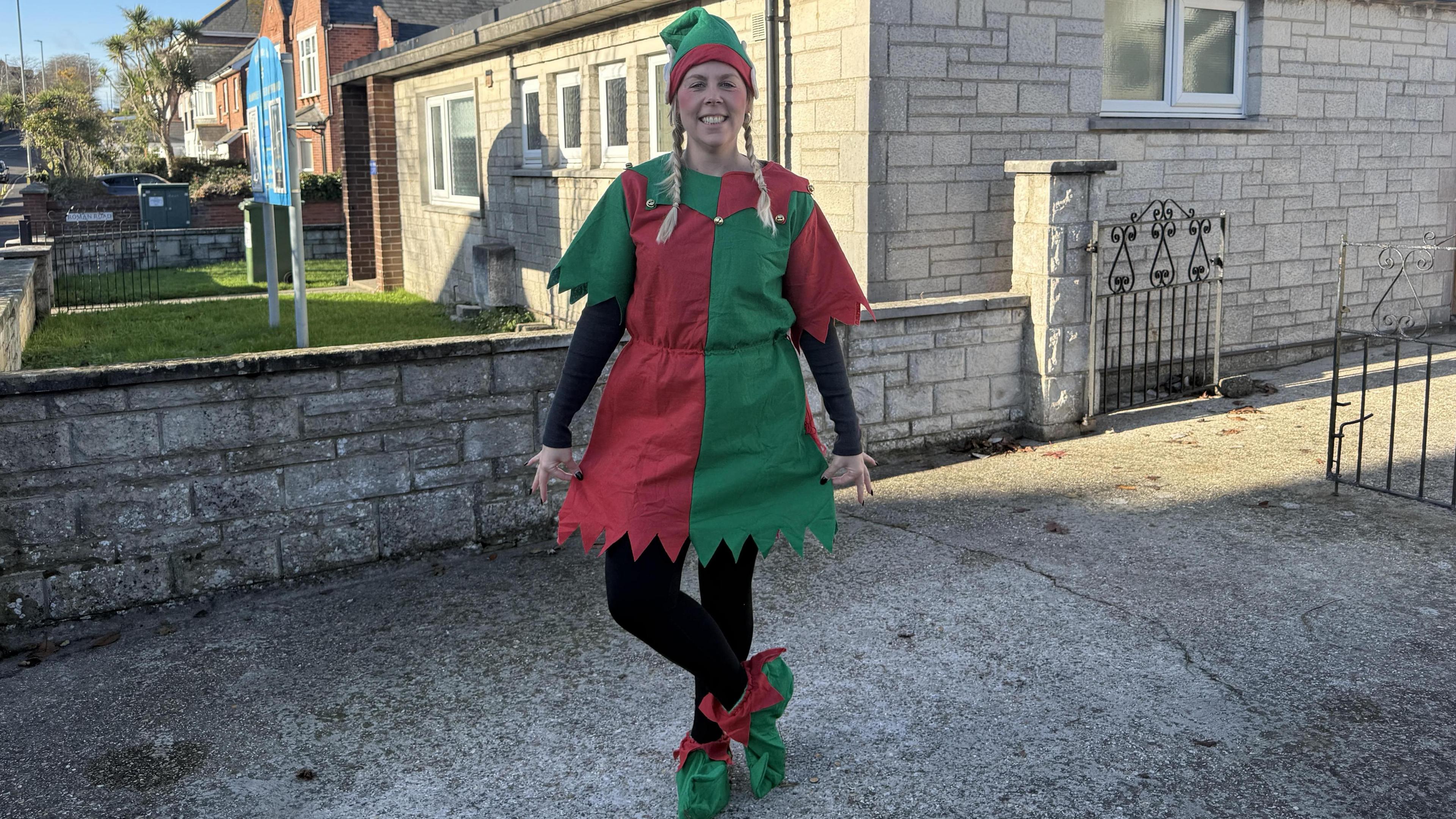 A woman smiling with blonde hair in plaits and wearing a green and red elf outfit.