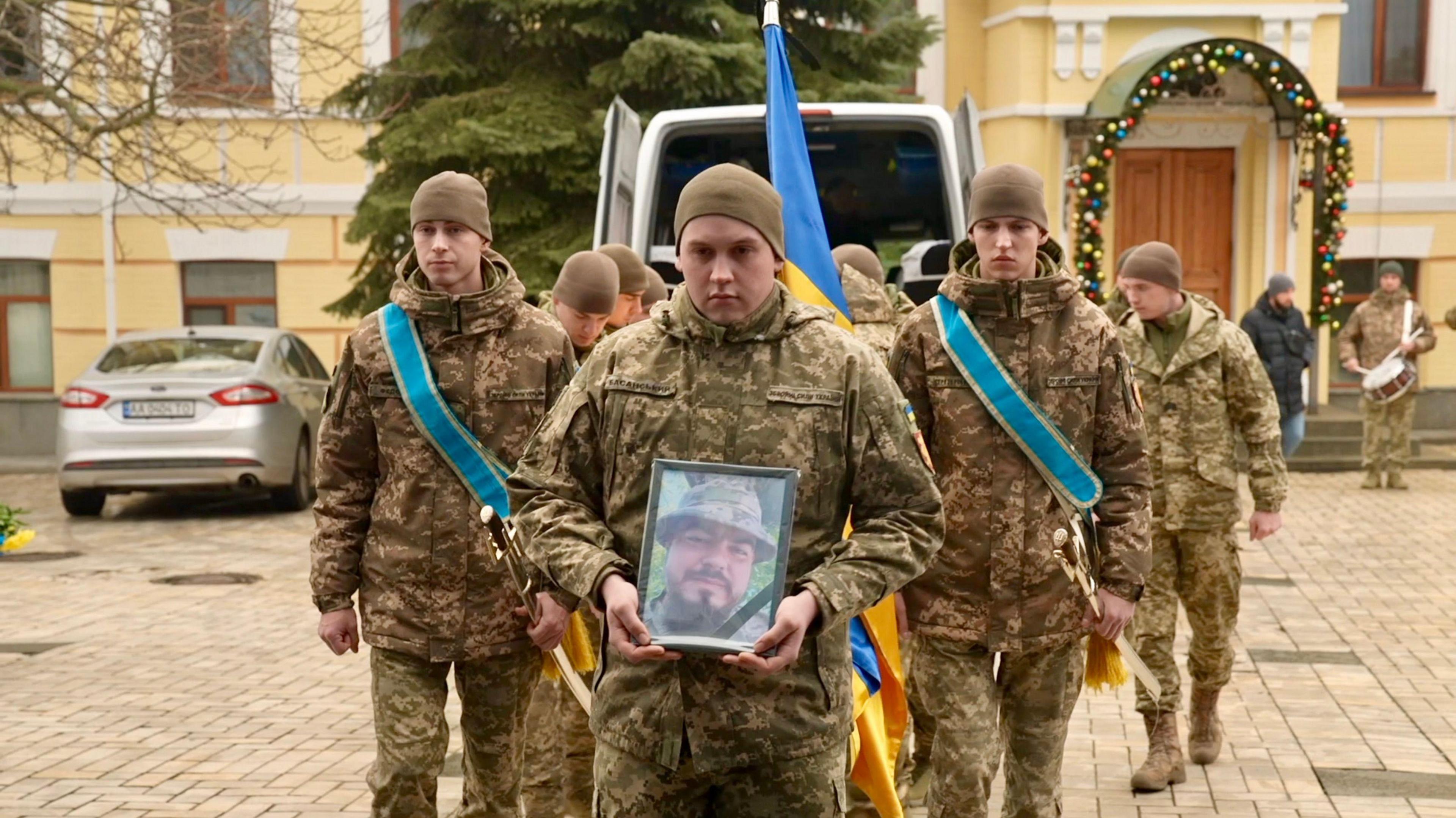 Soldiers hold a photo of Andriy Kusmenko outside the location of his funeral