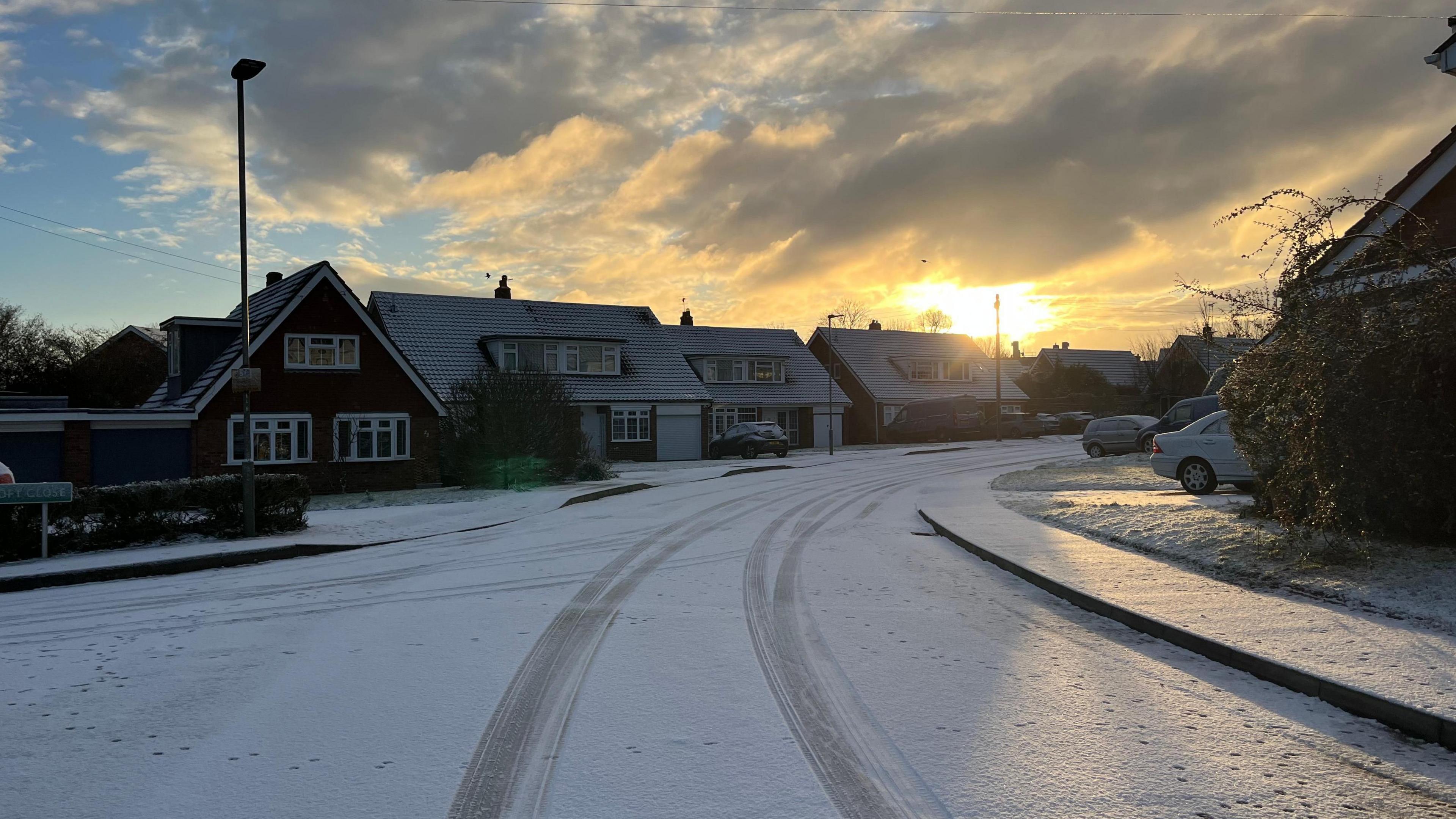 Residential street at sunrise, with road and pavement dusted in a thin layer of snow.