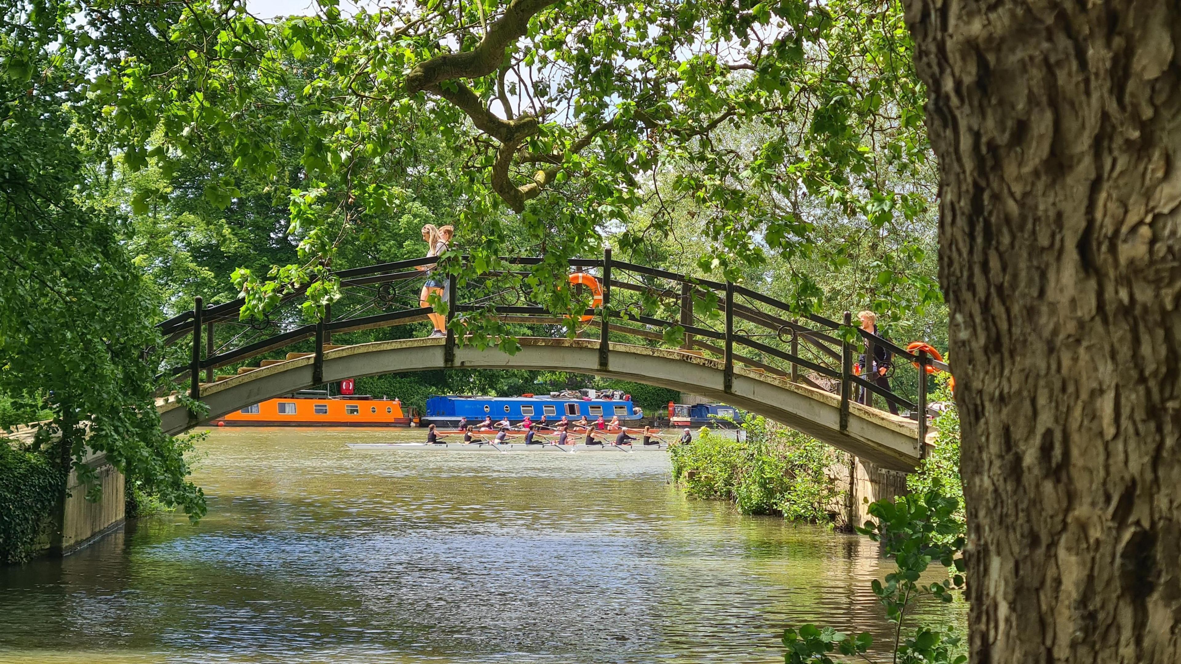 TUESDAY - Two people walk over a bridge over the Thames as a crew of rowers pass underneath