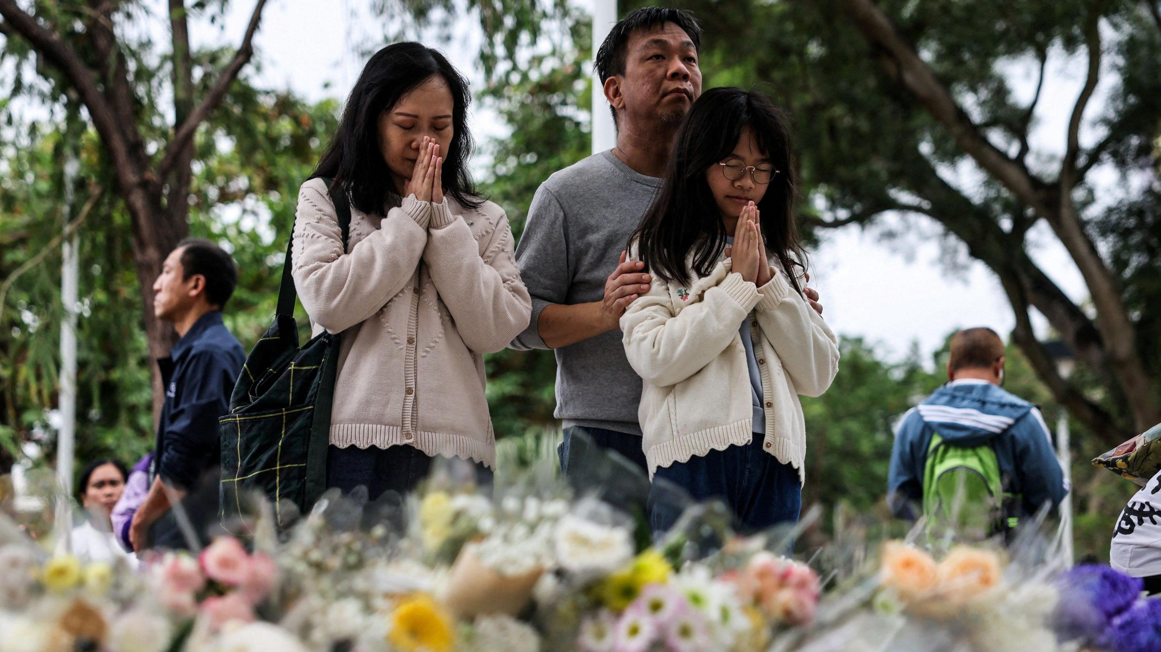 People praying as they stand in front of flowers laid on the ground as tribute to the victims of the fire