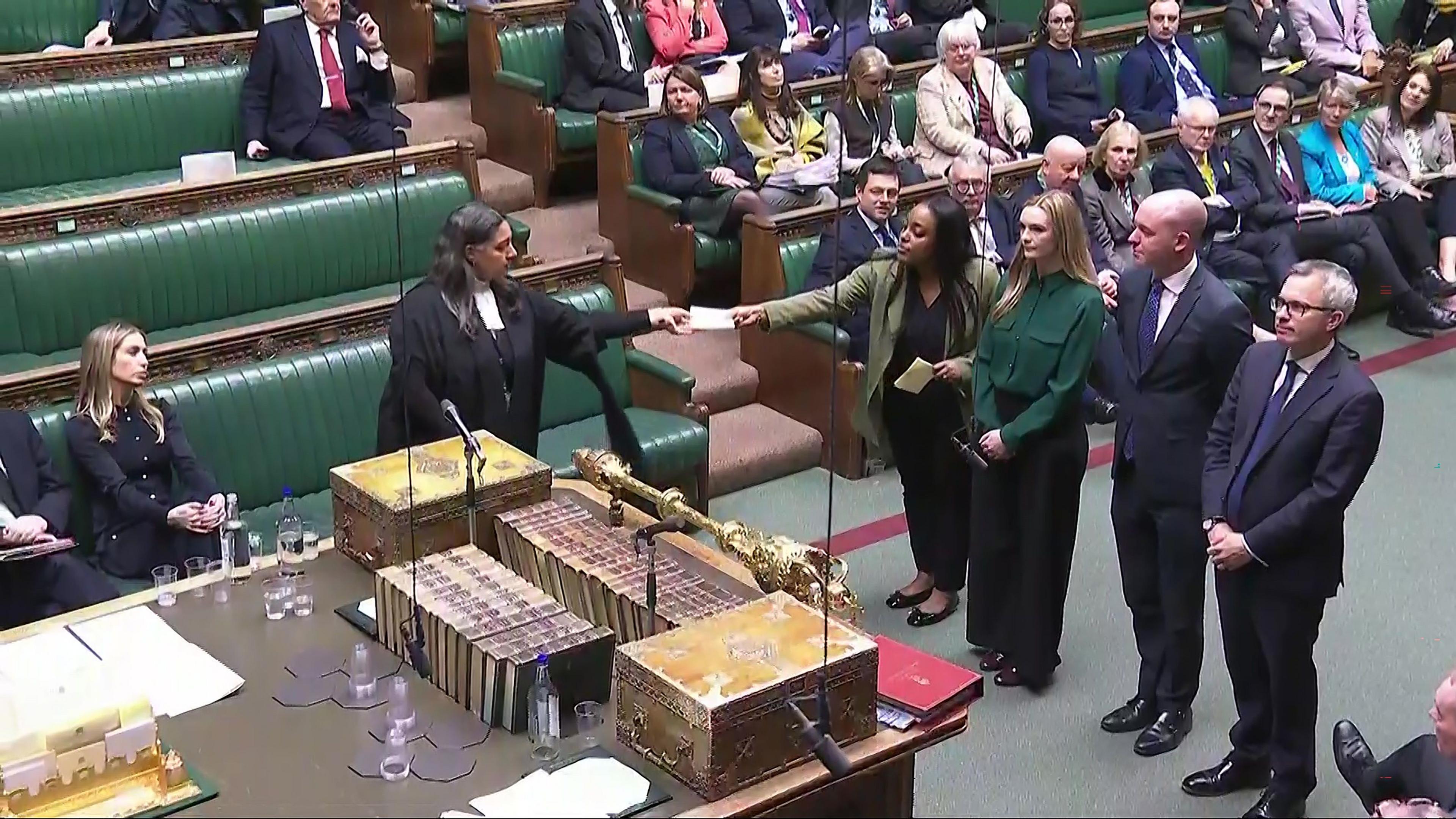 Four MPs line up side-by-side on the floor of the House of Commons to hand the result of a vote to a clerk. 