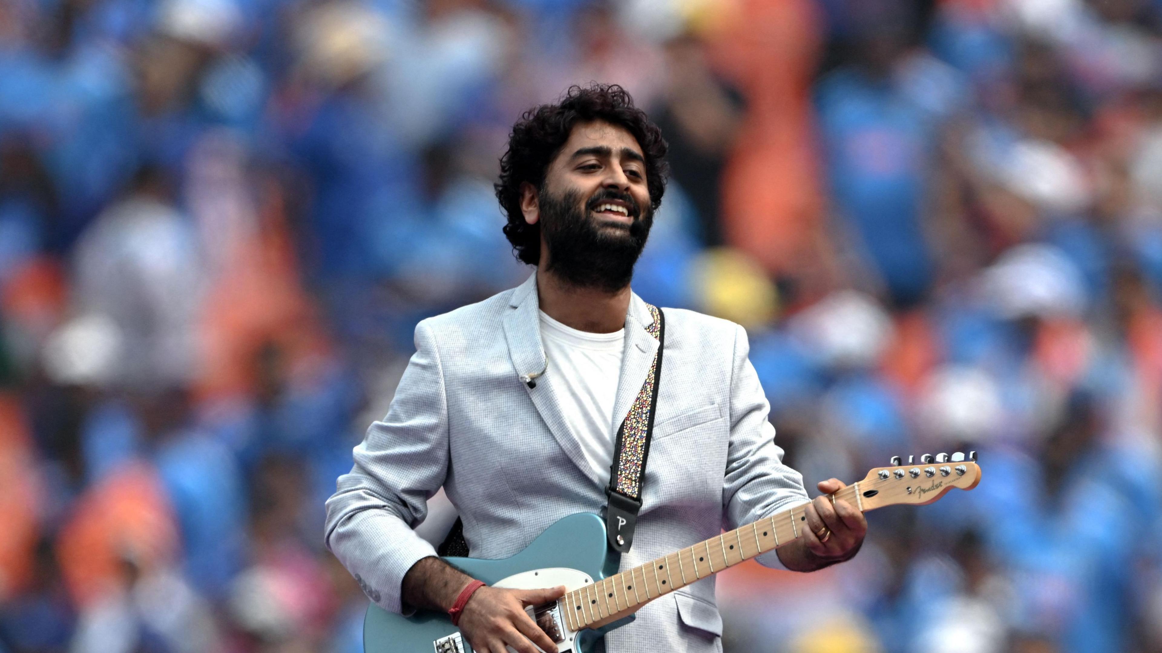 Arijit Singh holding a guitar and singing at a concert.