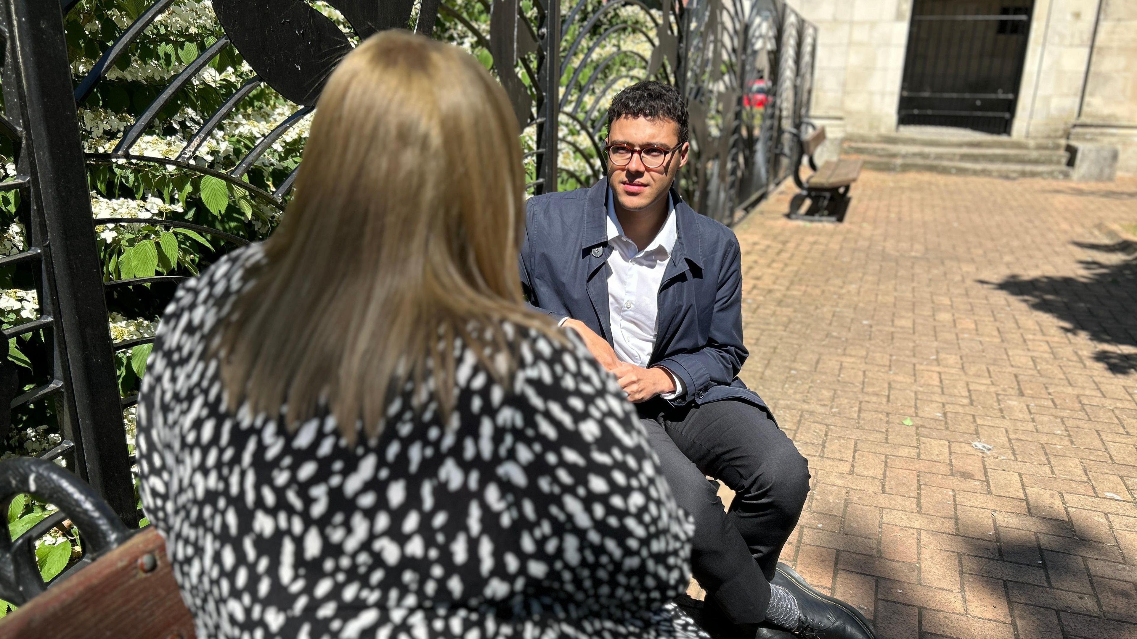 BBC reporter Josh Sandiford speaks to the anonymous mother of a Swinfen Hall prisoner. He is wearing a blue jacket and a white shirt. She has a black and white dress on. We can only see the back of her head