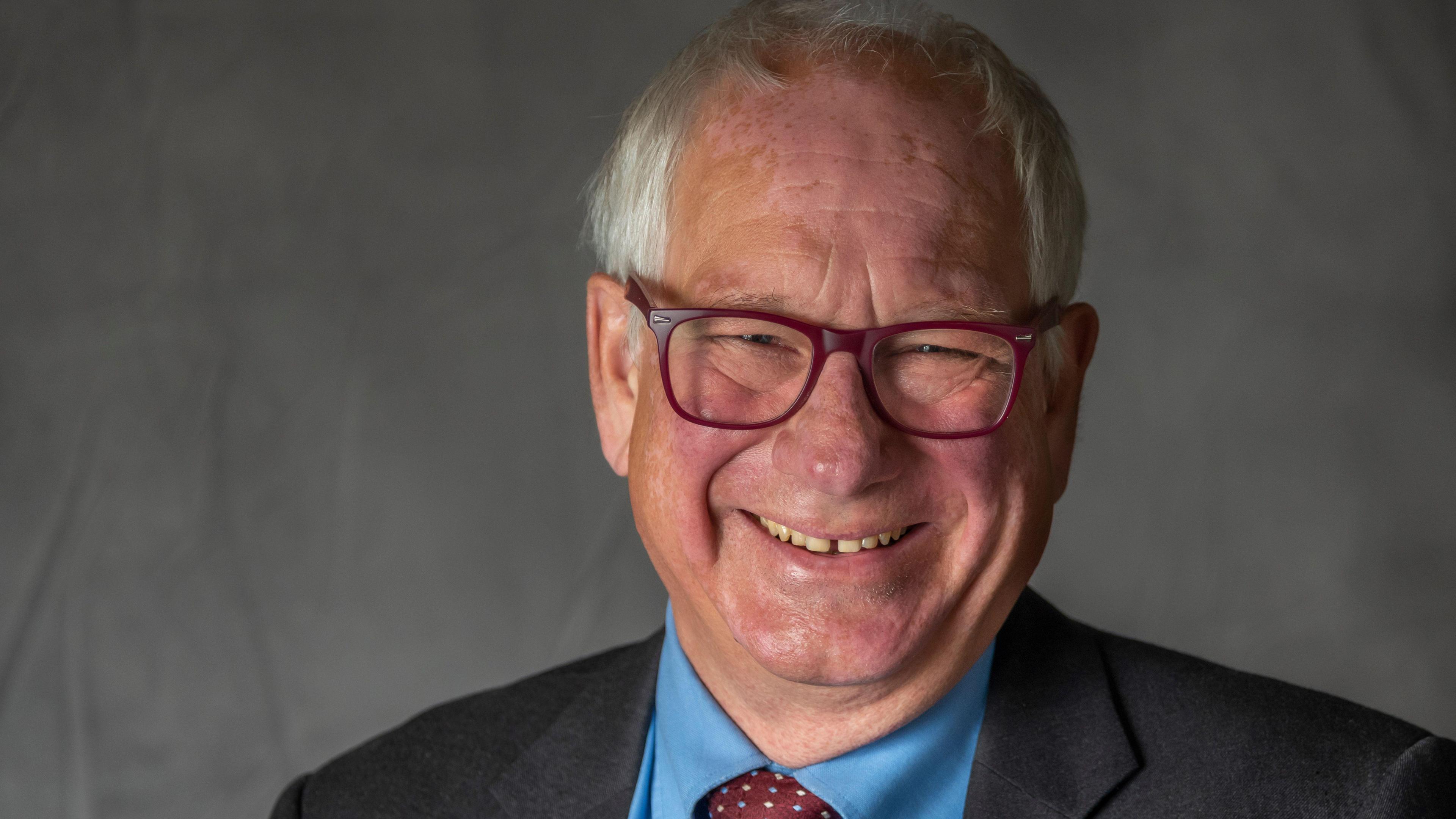 A head and shoulders photograph of Councillor Richard Cleaver, a man with white hair who wears glasses, a dark suit, a blue shirt and a red tie with white dots.