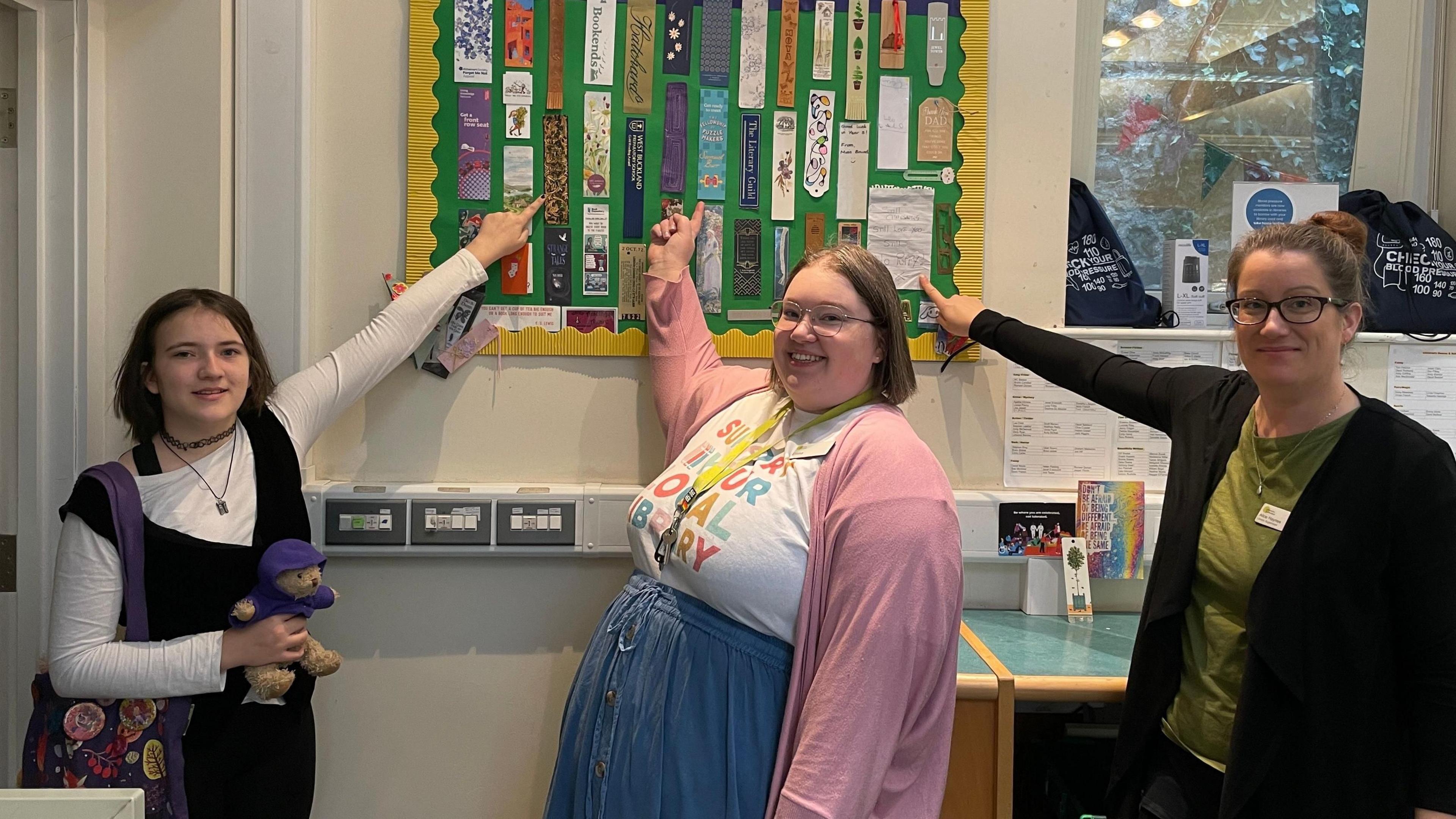 A girl, and two women stand in front of the bookmark display. They are all pointing to their favourites.
