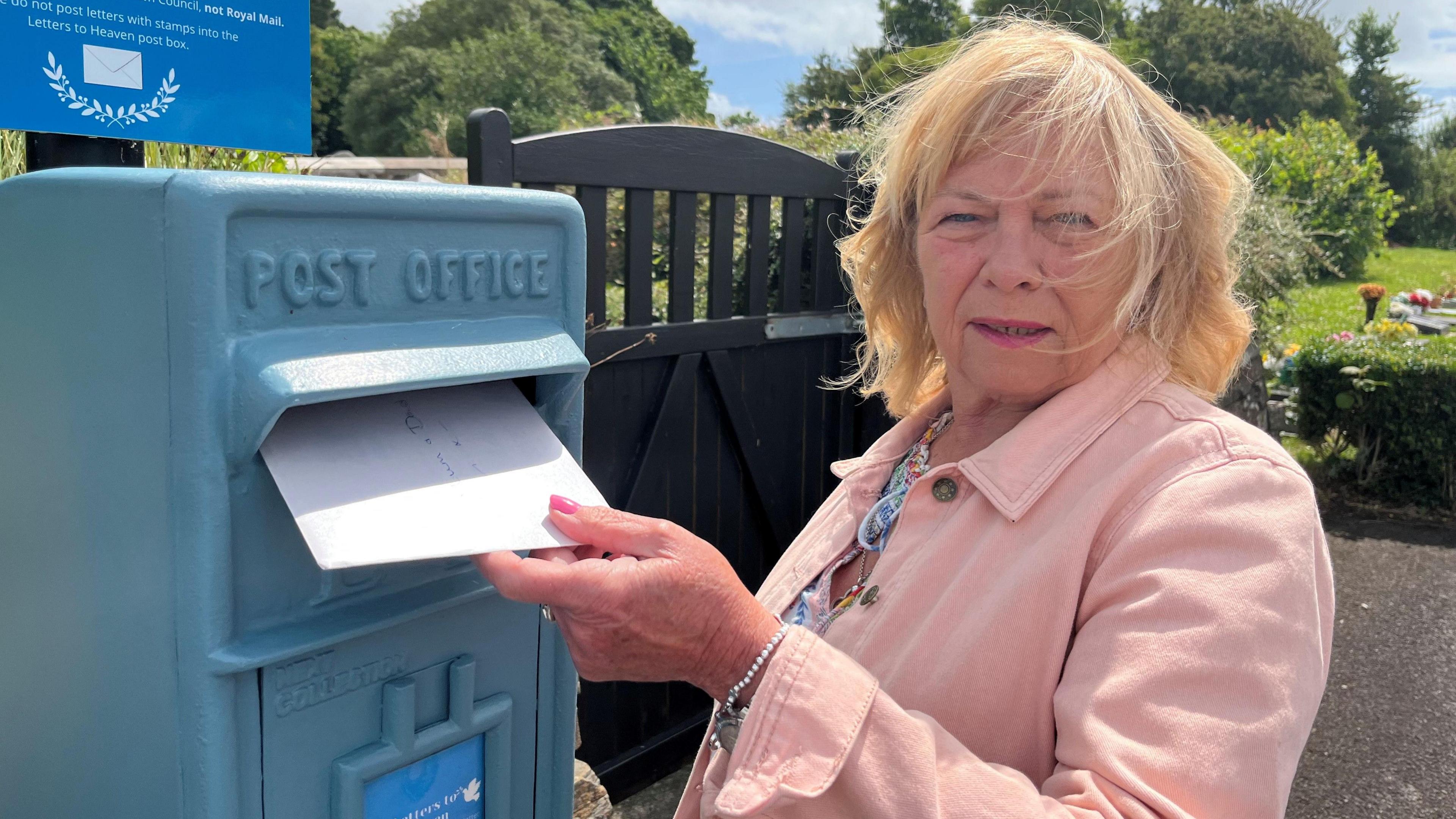 A woman posts a letter in a bright blue postbox