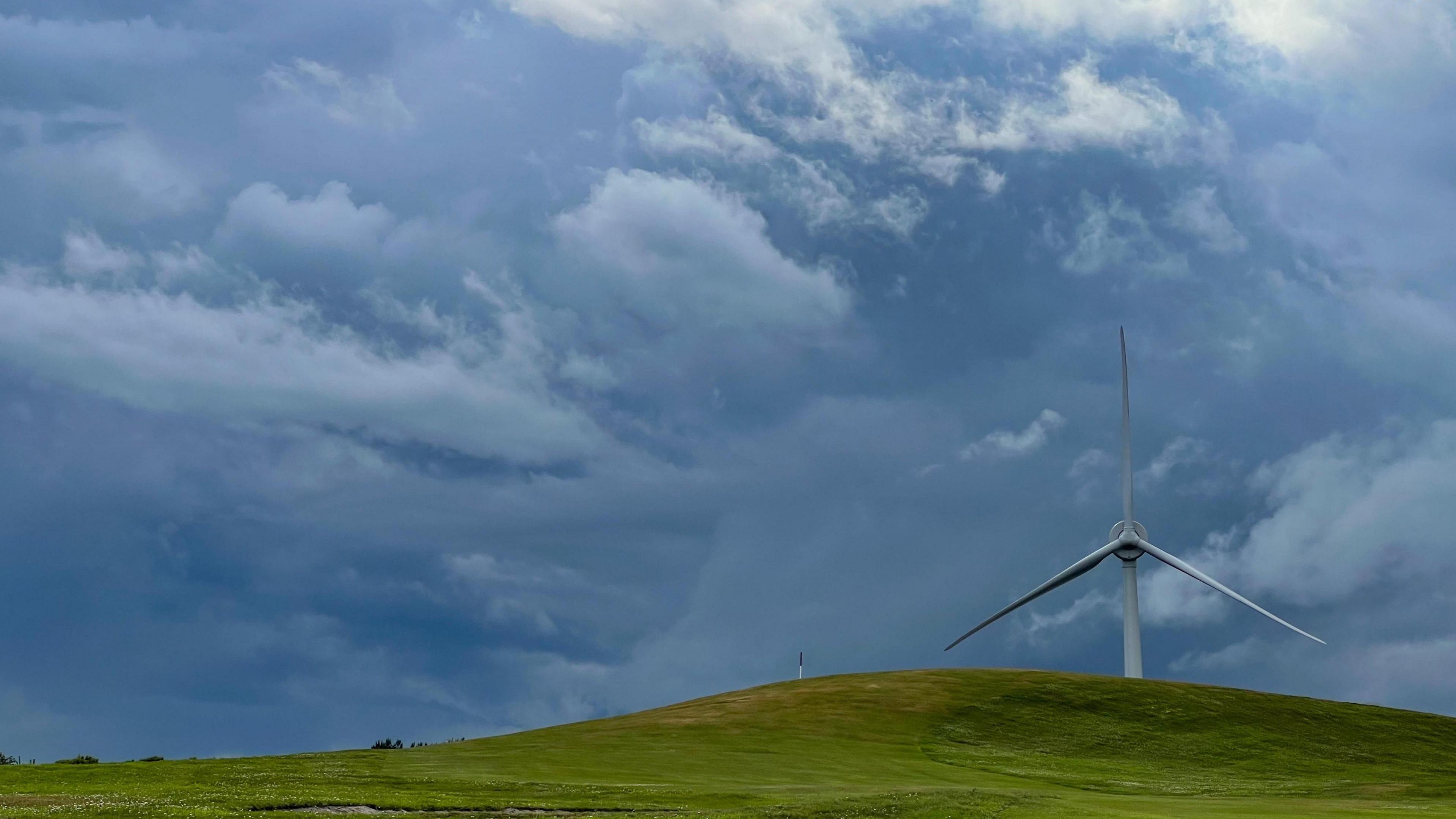 Dark clouds behind a hill and wind turbine