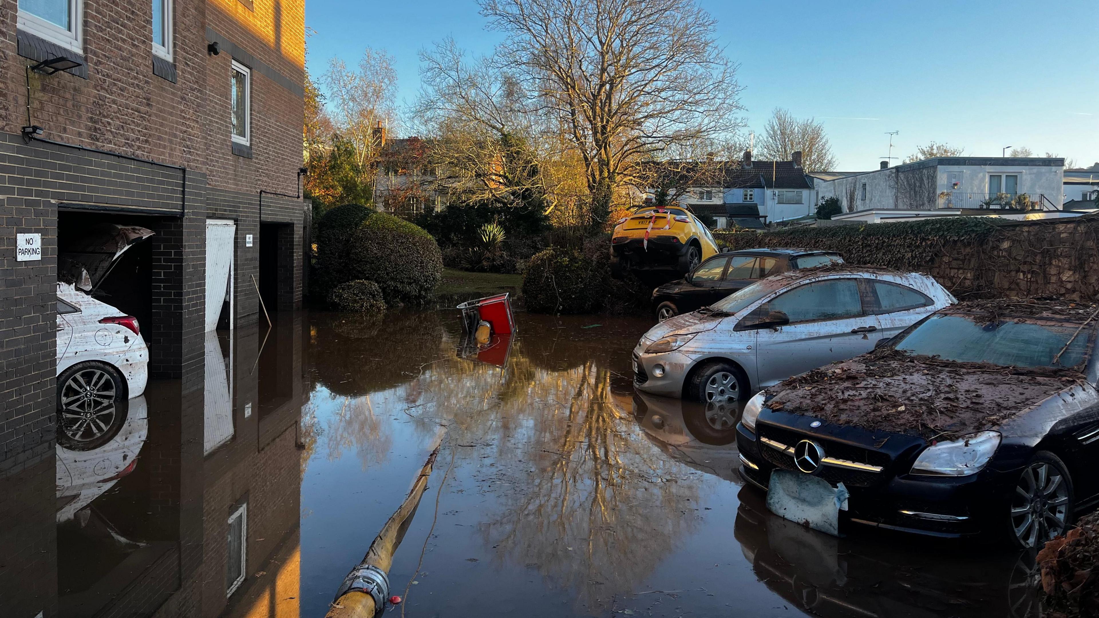 Three cars are parked outside residential homes submerged in flood water.