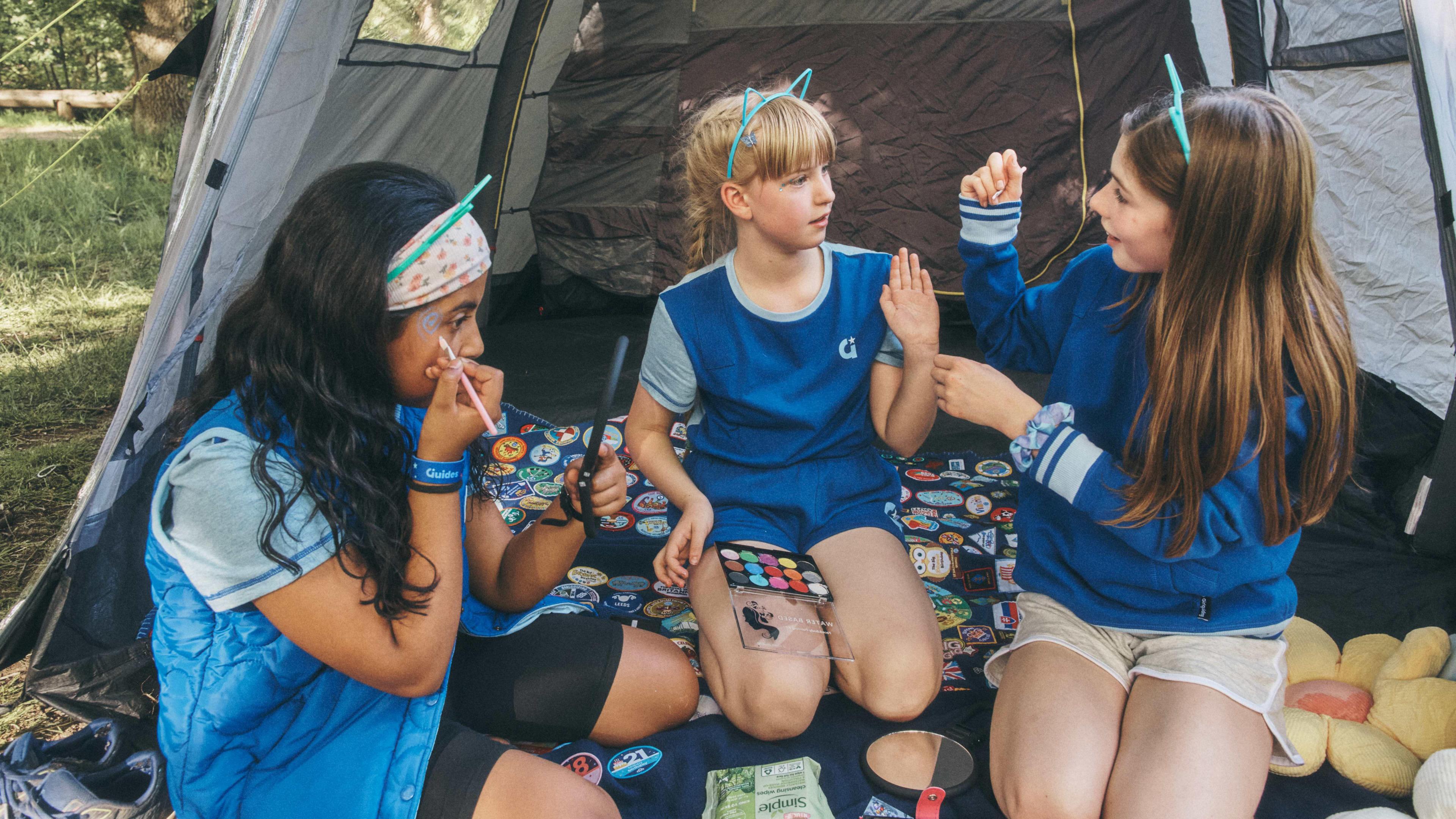 Three Guides in their new uniforms sitting outside a tent and putting face paint on.