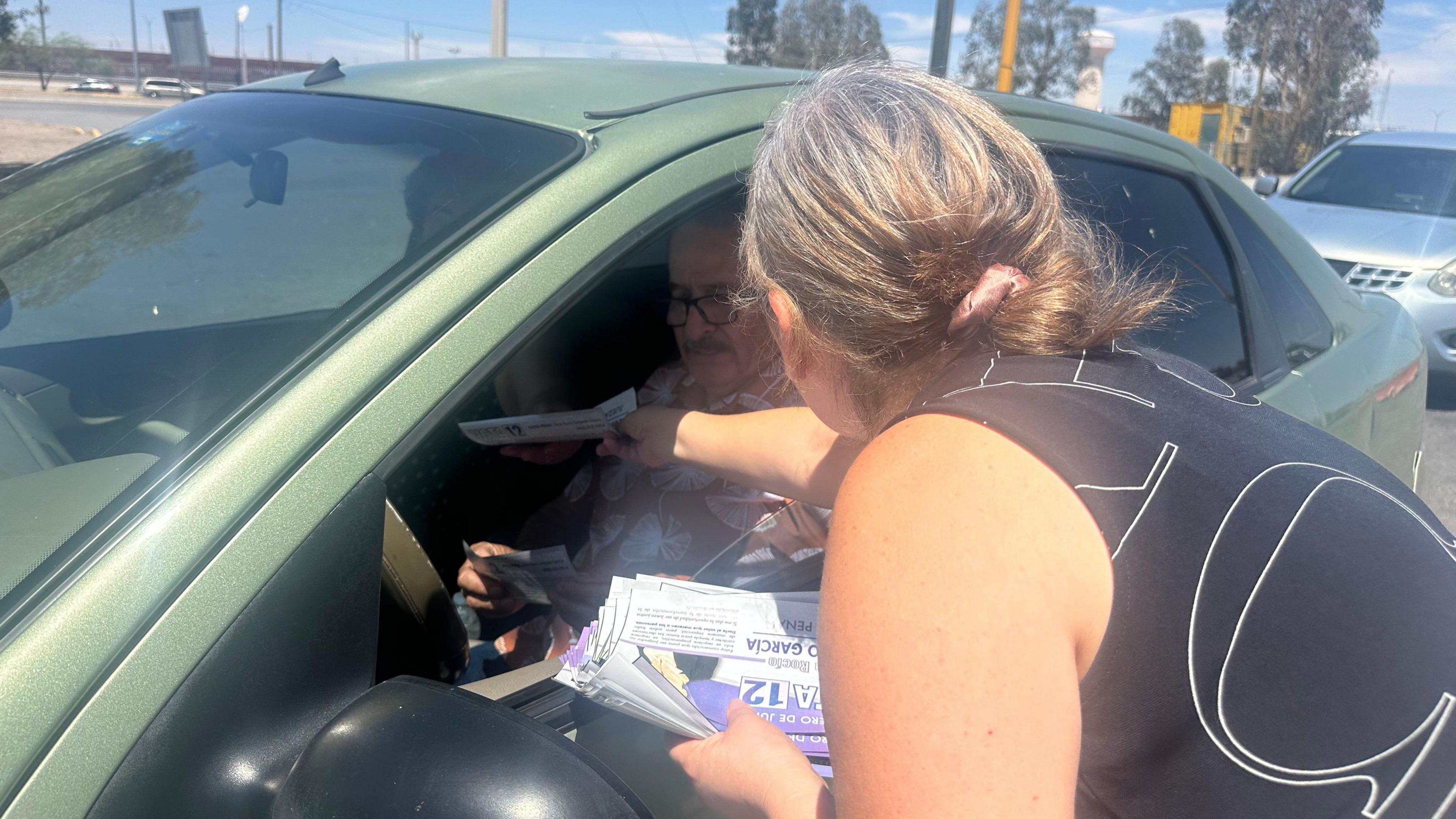 Silvia Delgado, wearing a black-and-white top, is handing out pamphlets to voters in a car at the Bridge of the Americas.