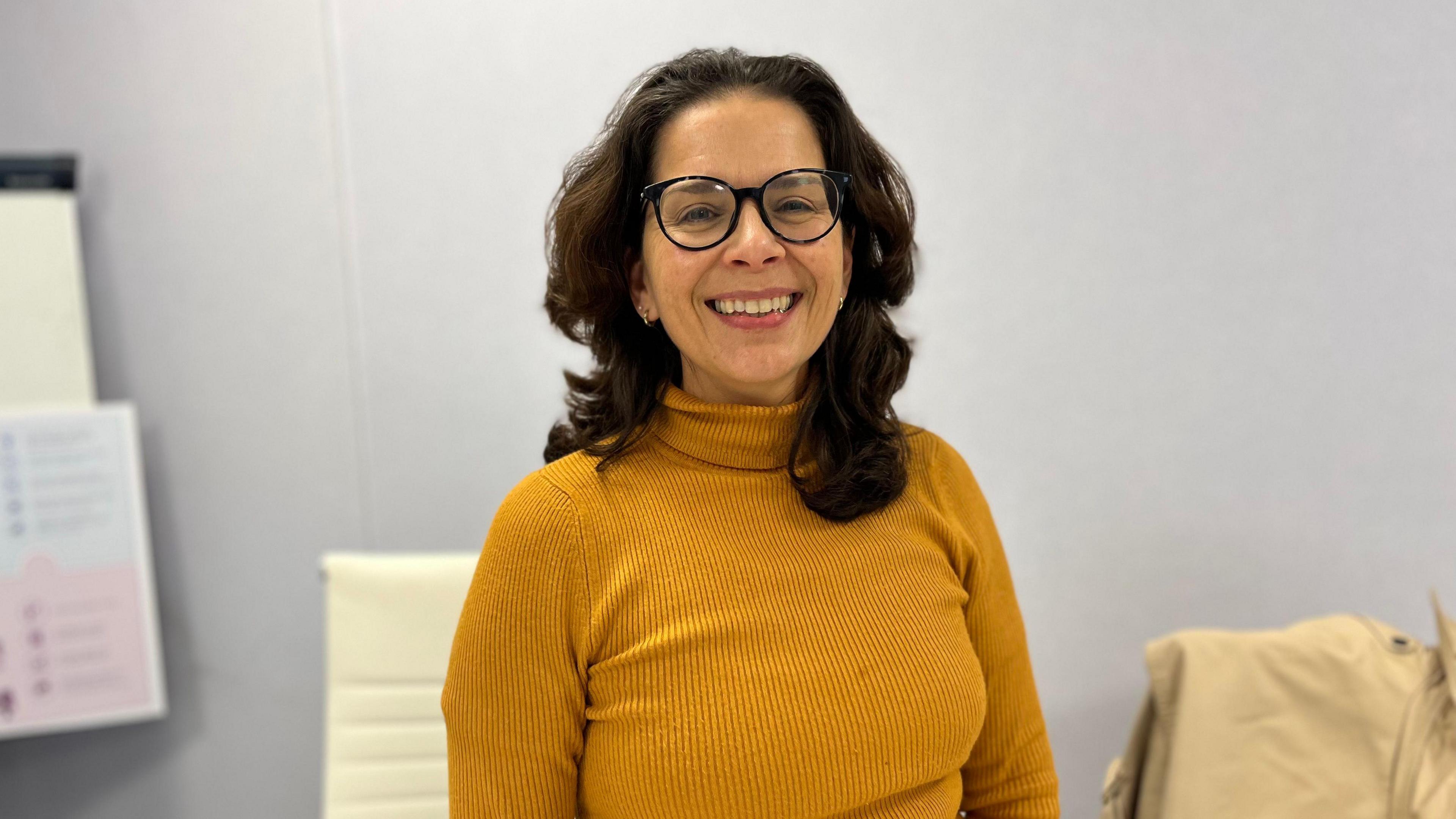 A picture of Education president Andrea Dudley-Owen. 
She is a women with dark brown mid length hair, wearing a mustard yellow high neck top. she has round glasses on and is smiling.