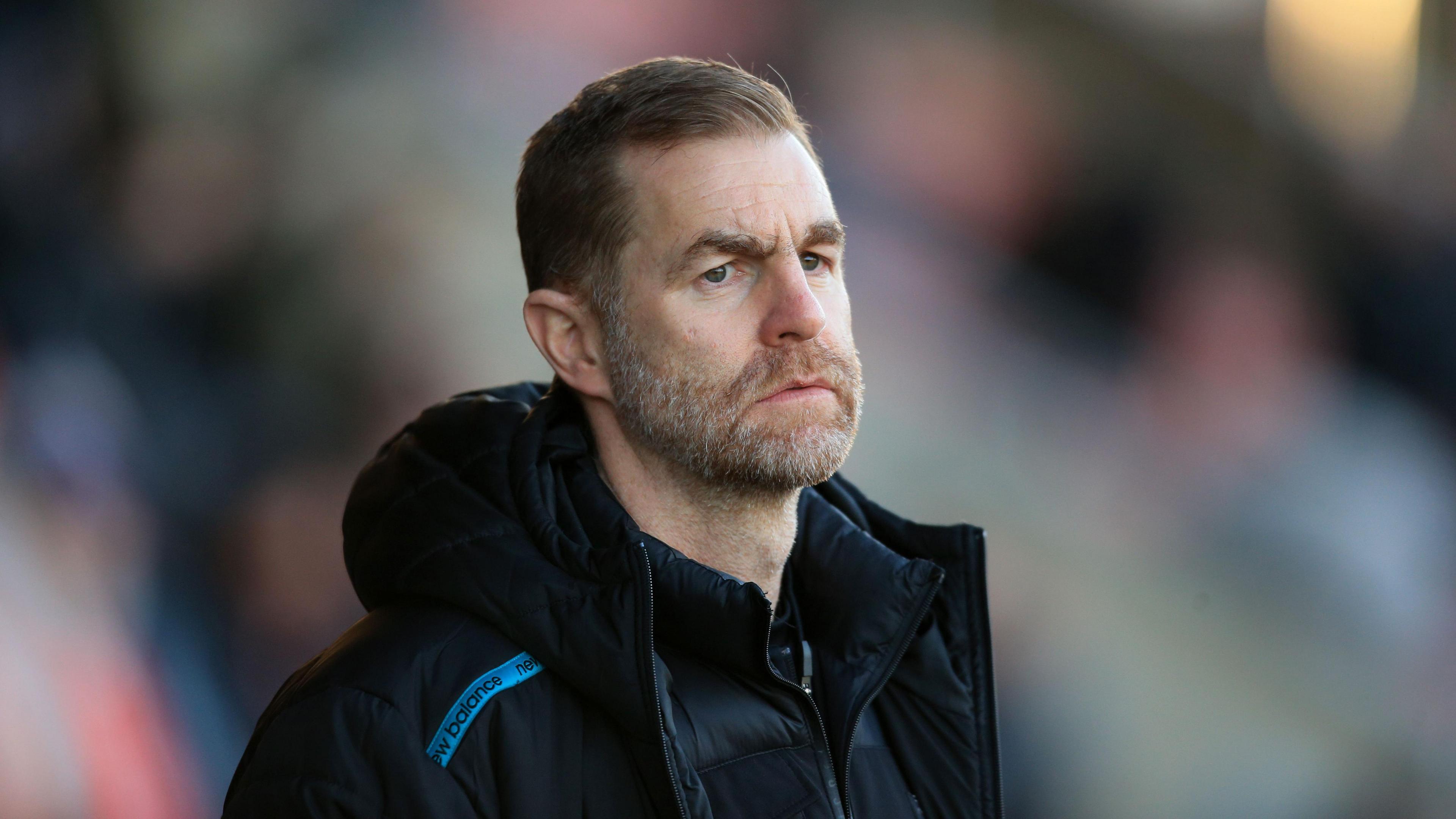 A close-up of Simon Weaver wearing a black New Balance jacket, looking concerned