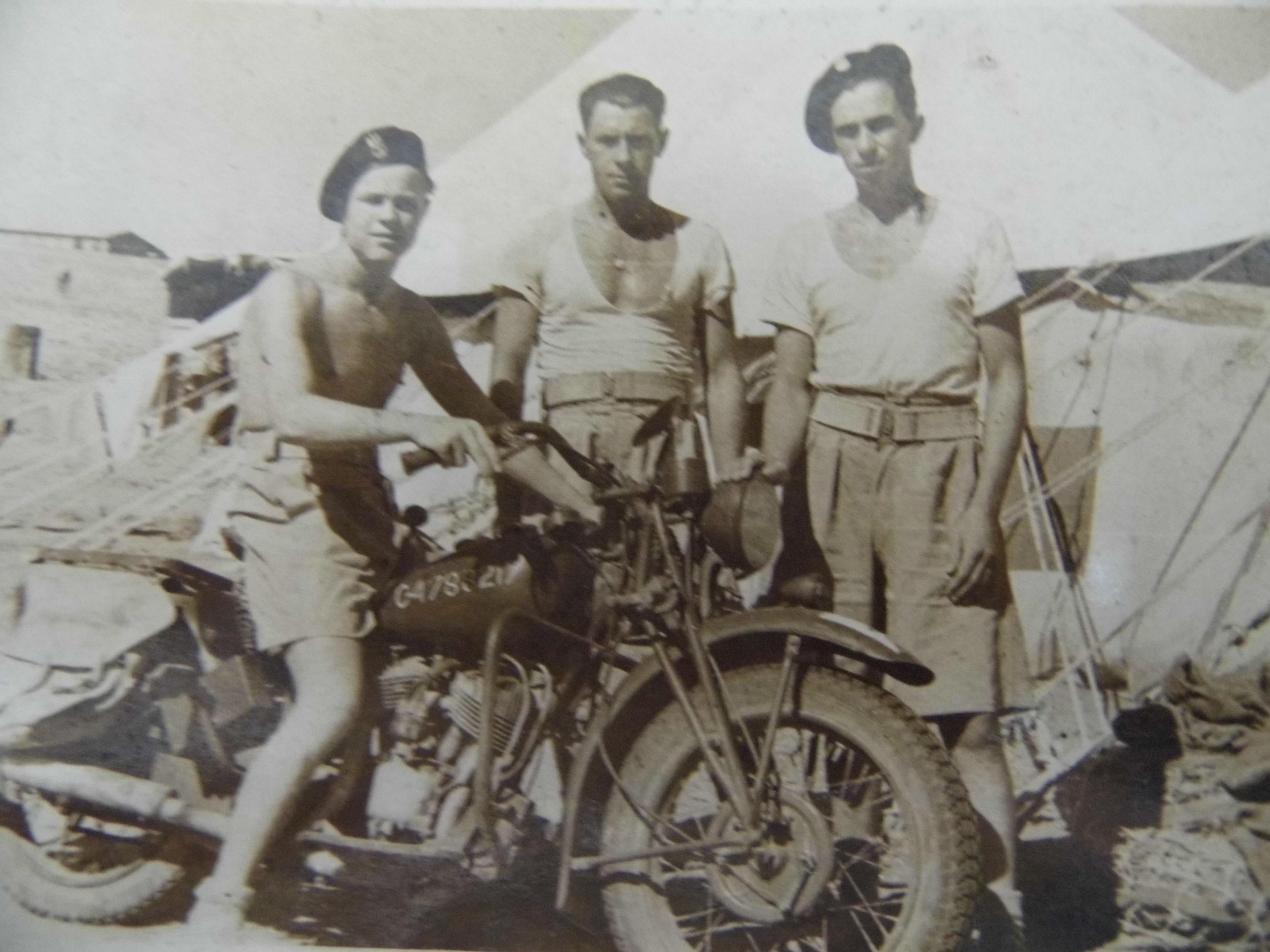 A shirtless Cpl Gasior of  2nd Polish Corps sits on his motorbike next to two other soldiers from the Polish Army 