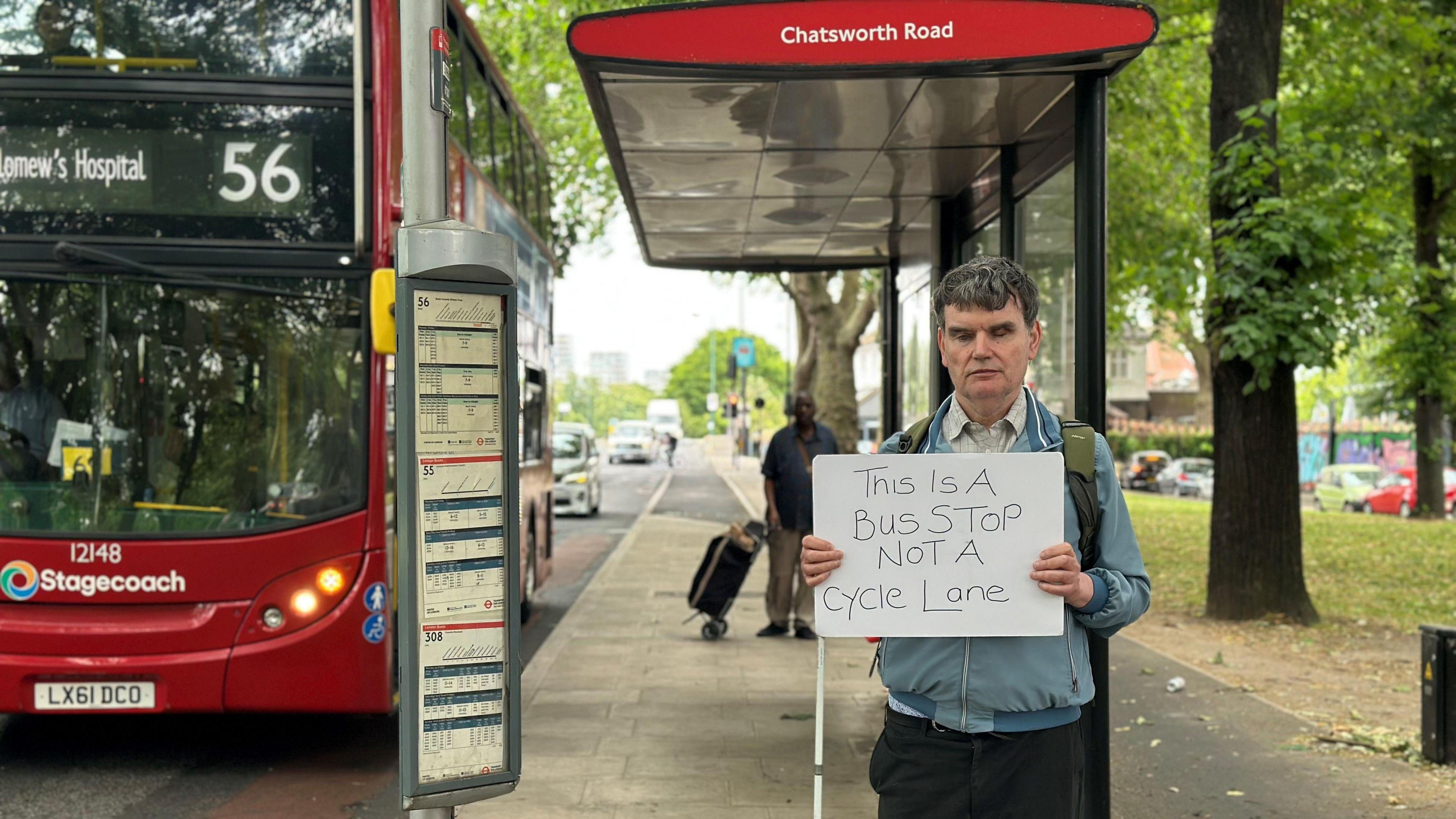 Andrew Hodgson holds a sign that reads 'This is a bus stop not a cycle lane' at a floating bus stop