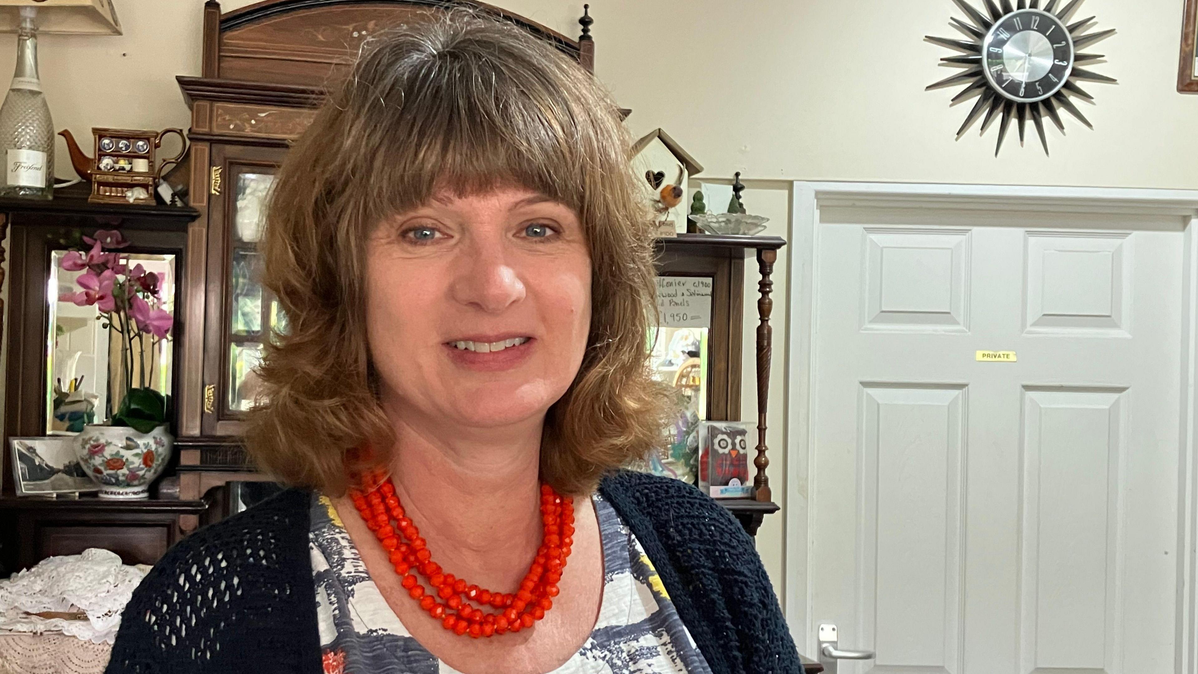 Woman wearing bright red bead necklace stands in a shop