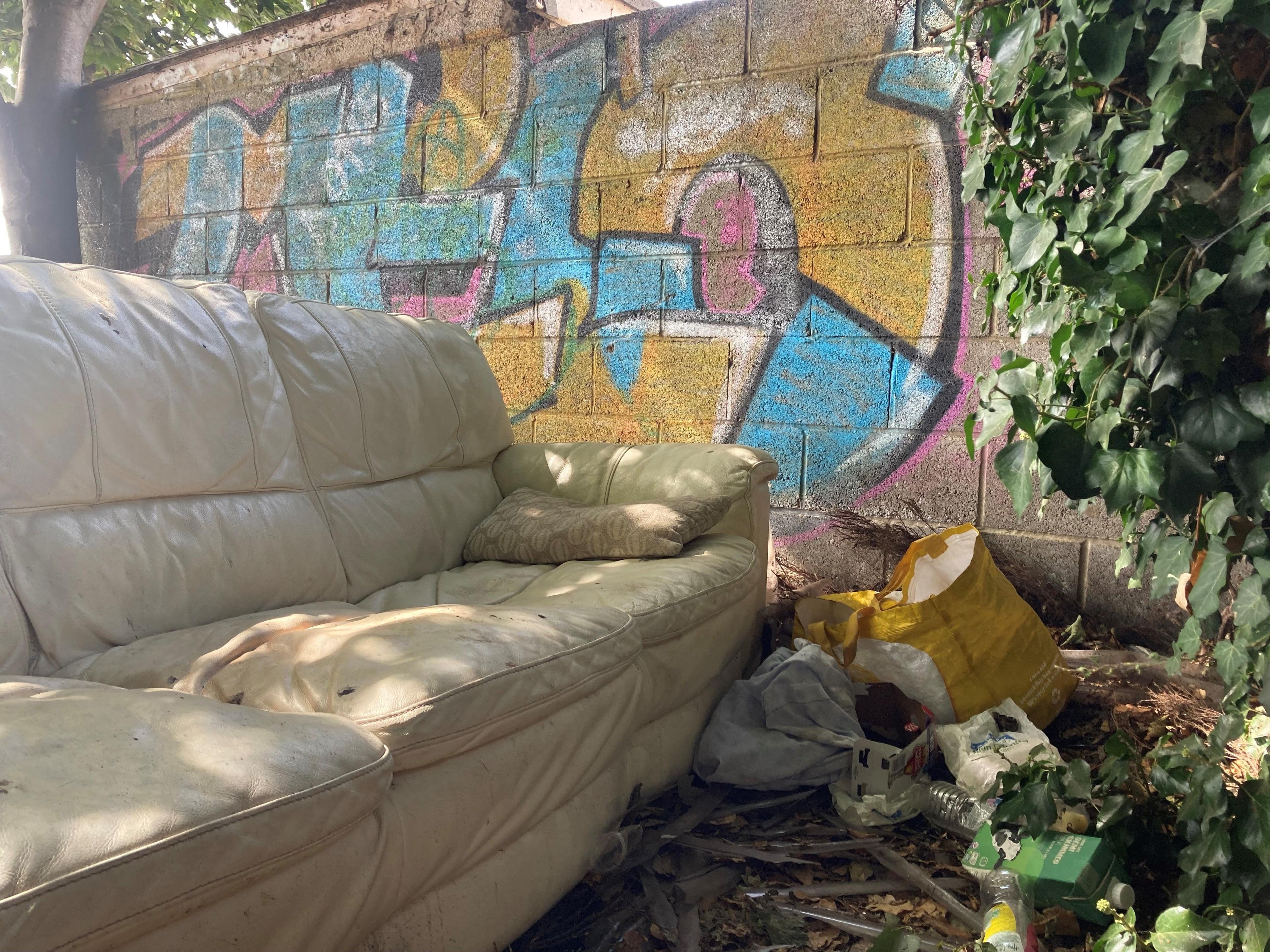 A sofa which has been dumped together with litter and a wall which has been sprayed with graffiti 