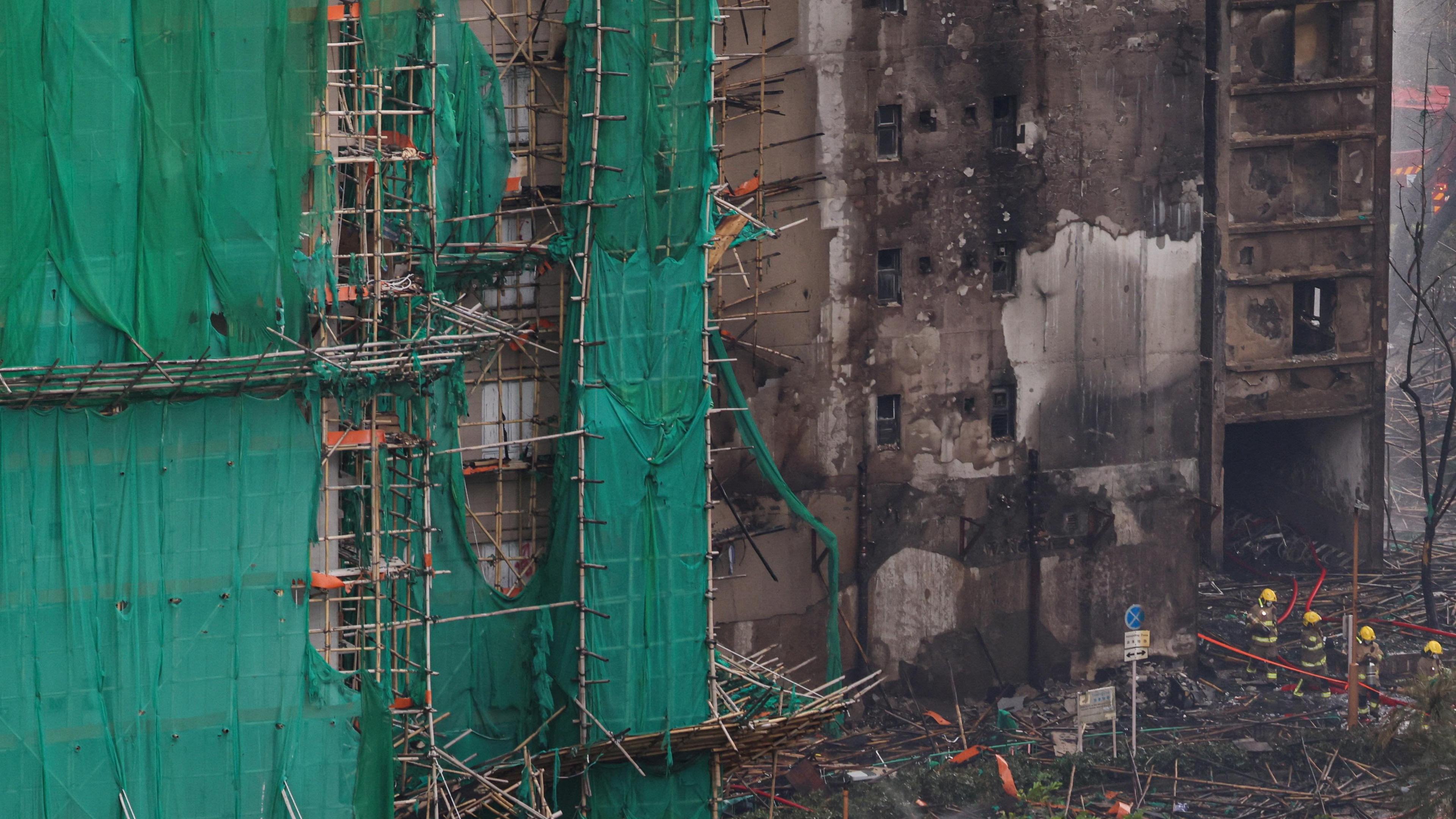 Firefighters walk past charred bamboo scaffolding at Wang Fuk Court after a fire