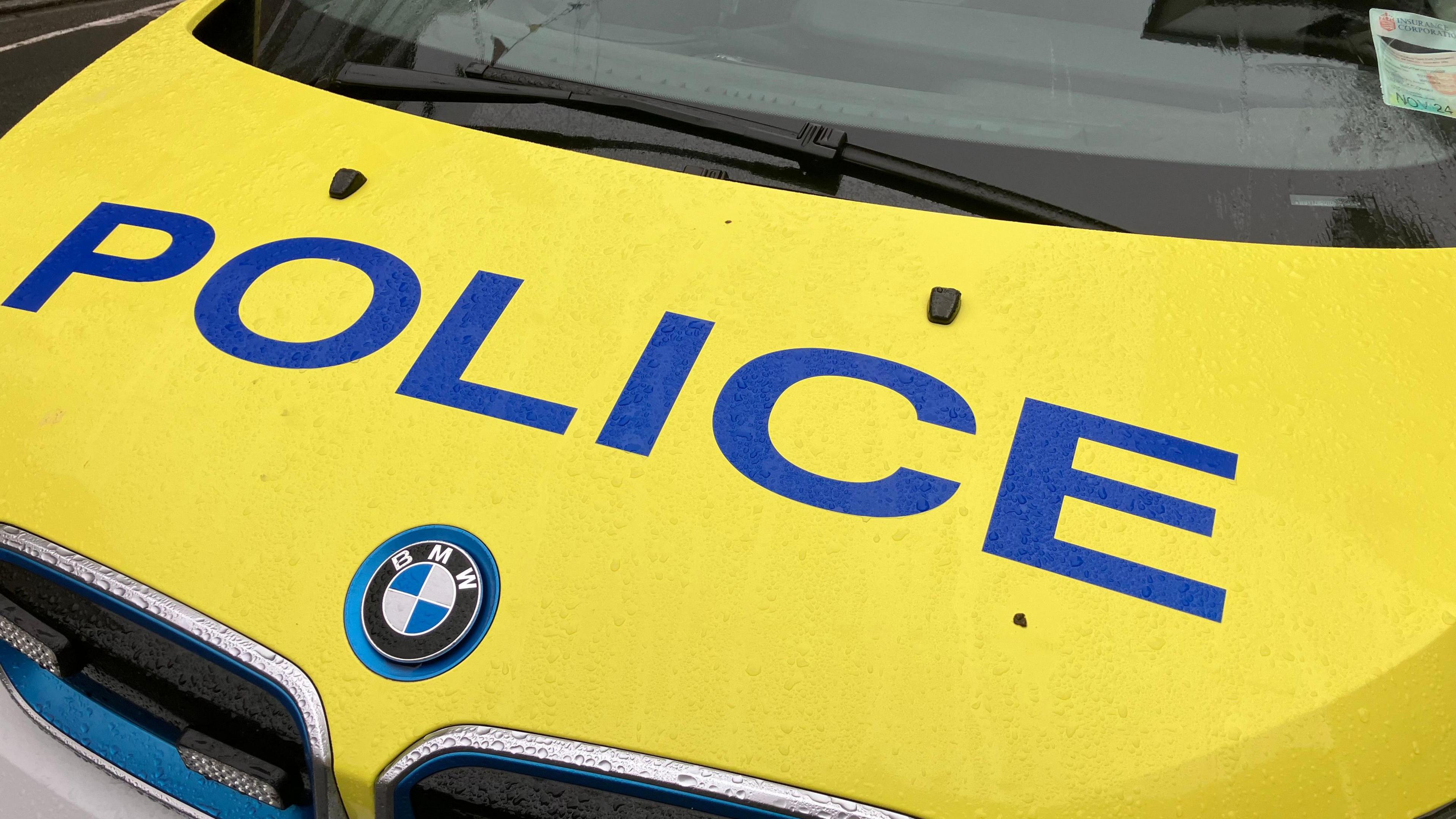 The bonnet of a Guernsey Police car. The bonnet is yellow with the words 'POLICE' in blue writing. There is a 'BMW' badge underneath. 