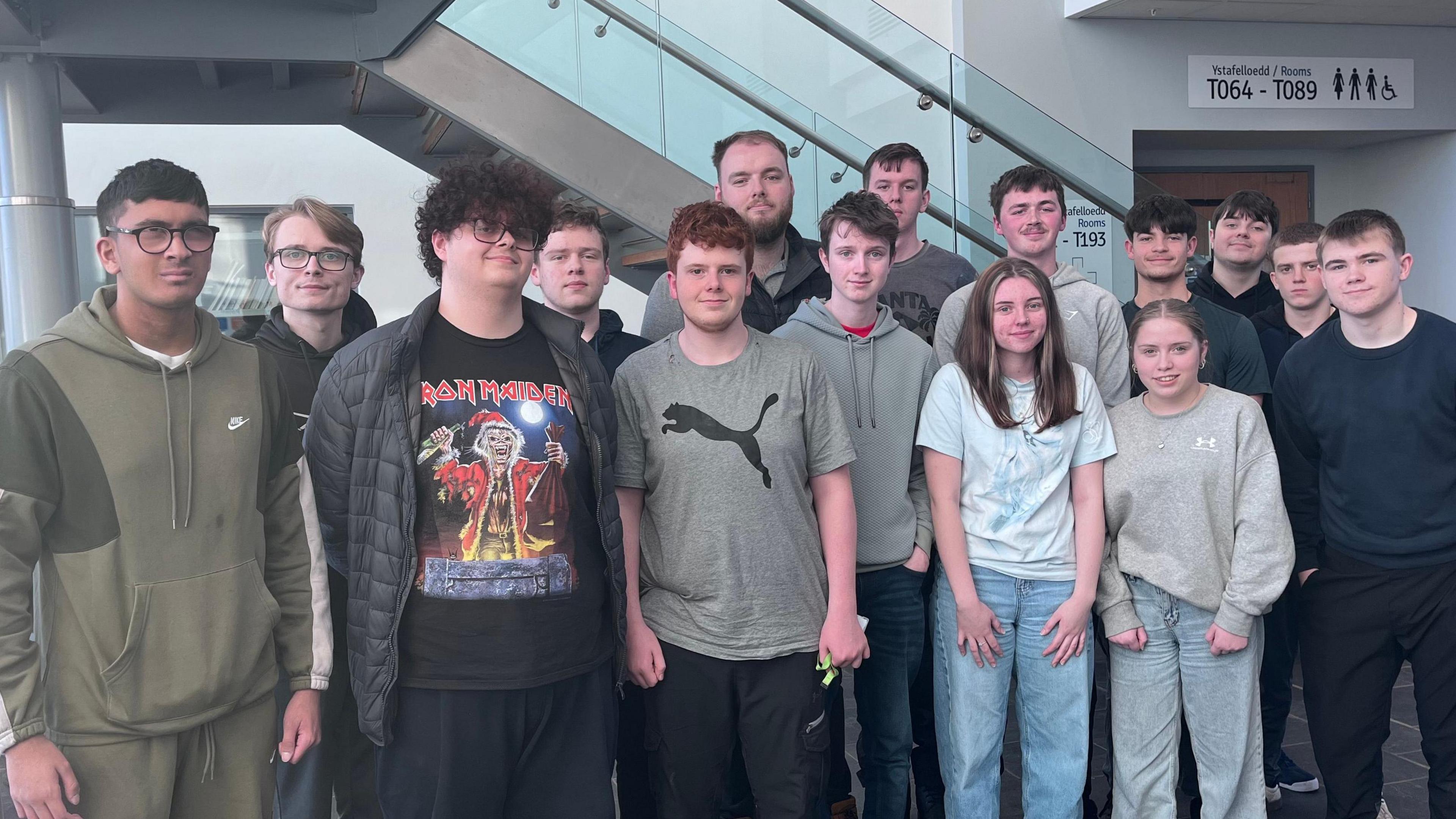 Grwp o 15 o bobol ifanc yn sefyll gyda'i gilydd mewn adeilad coleg