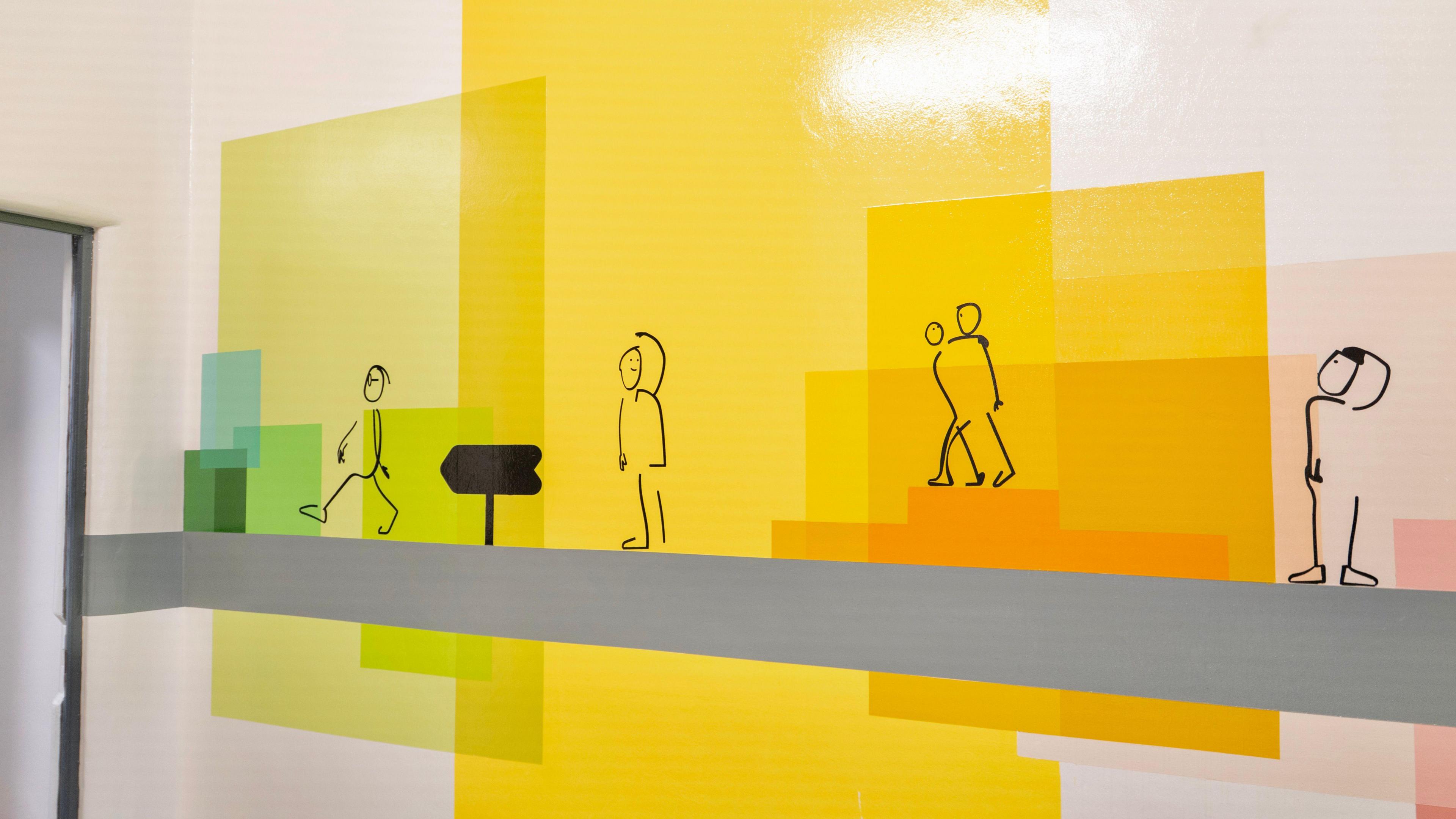 The design on the custody suite wall features colourful squares and stick figure people in various poses.