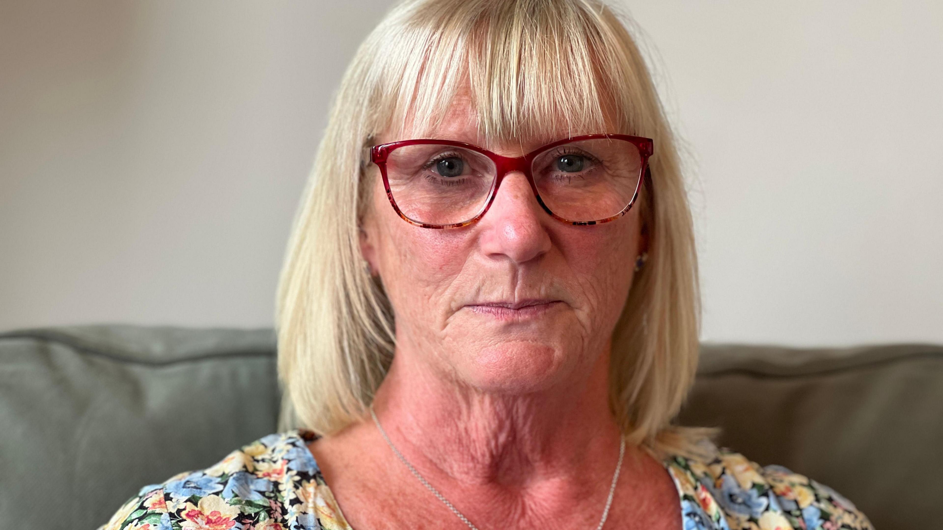 A woman with blonde hair and red-rimmed spectacles stares into the camera.