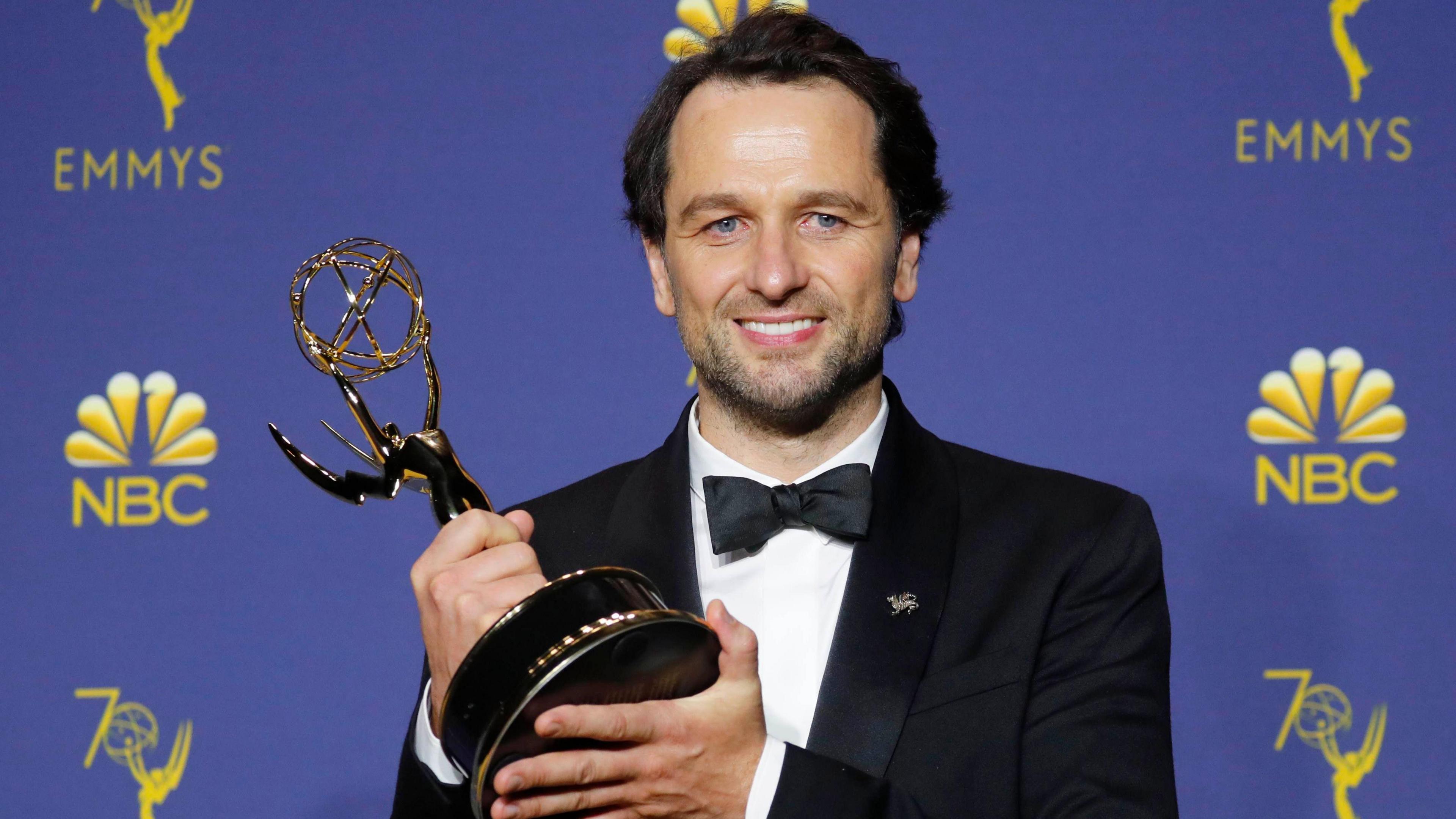 Matthew Rhys, in black tie, smiles at the camera with the Emmy he won in 2018