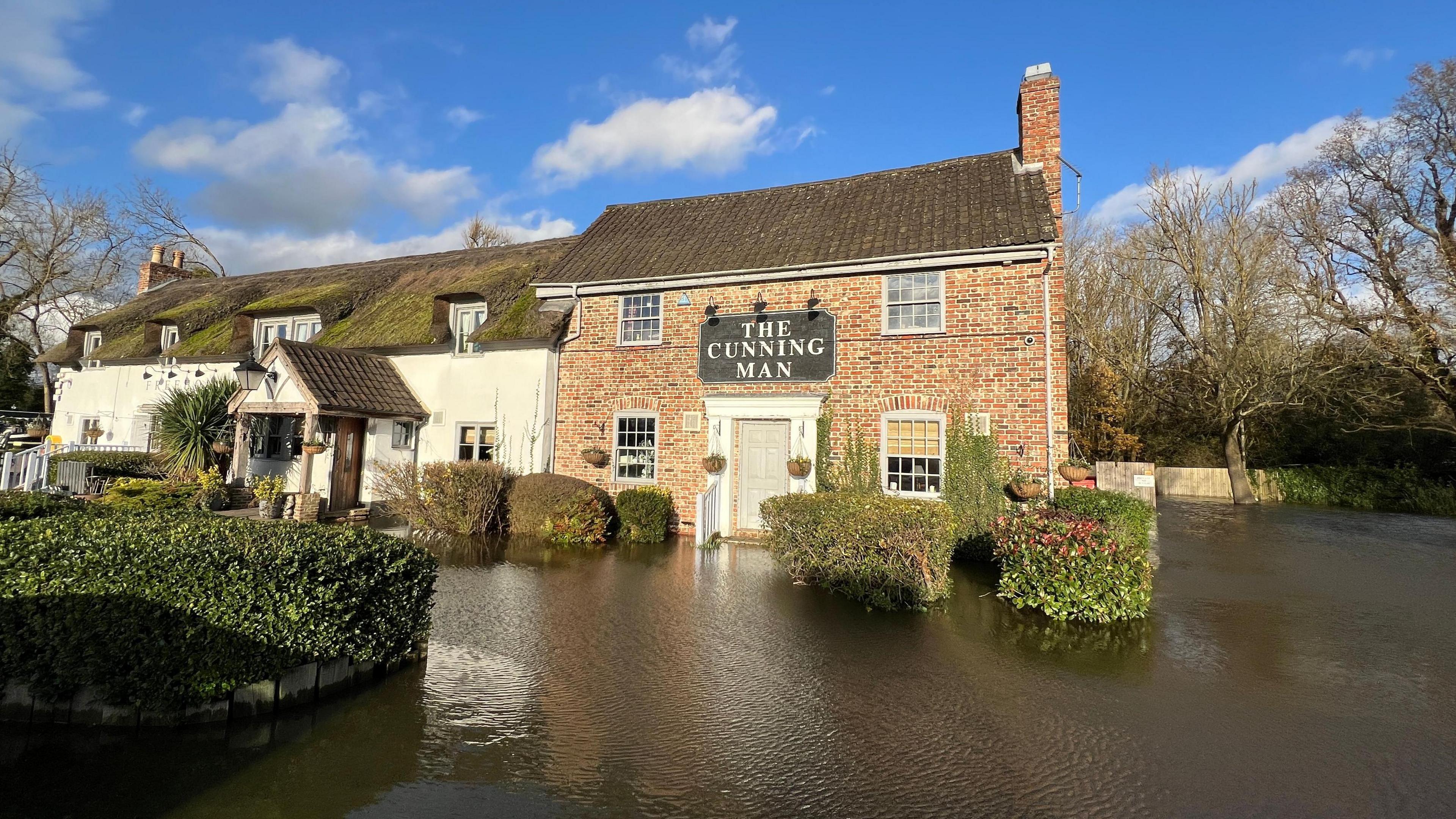 A general view picture of The Cunning Man, a two-storey building with a large black sign that says "The Cunning Man"