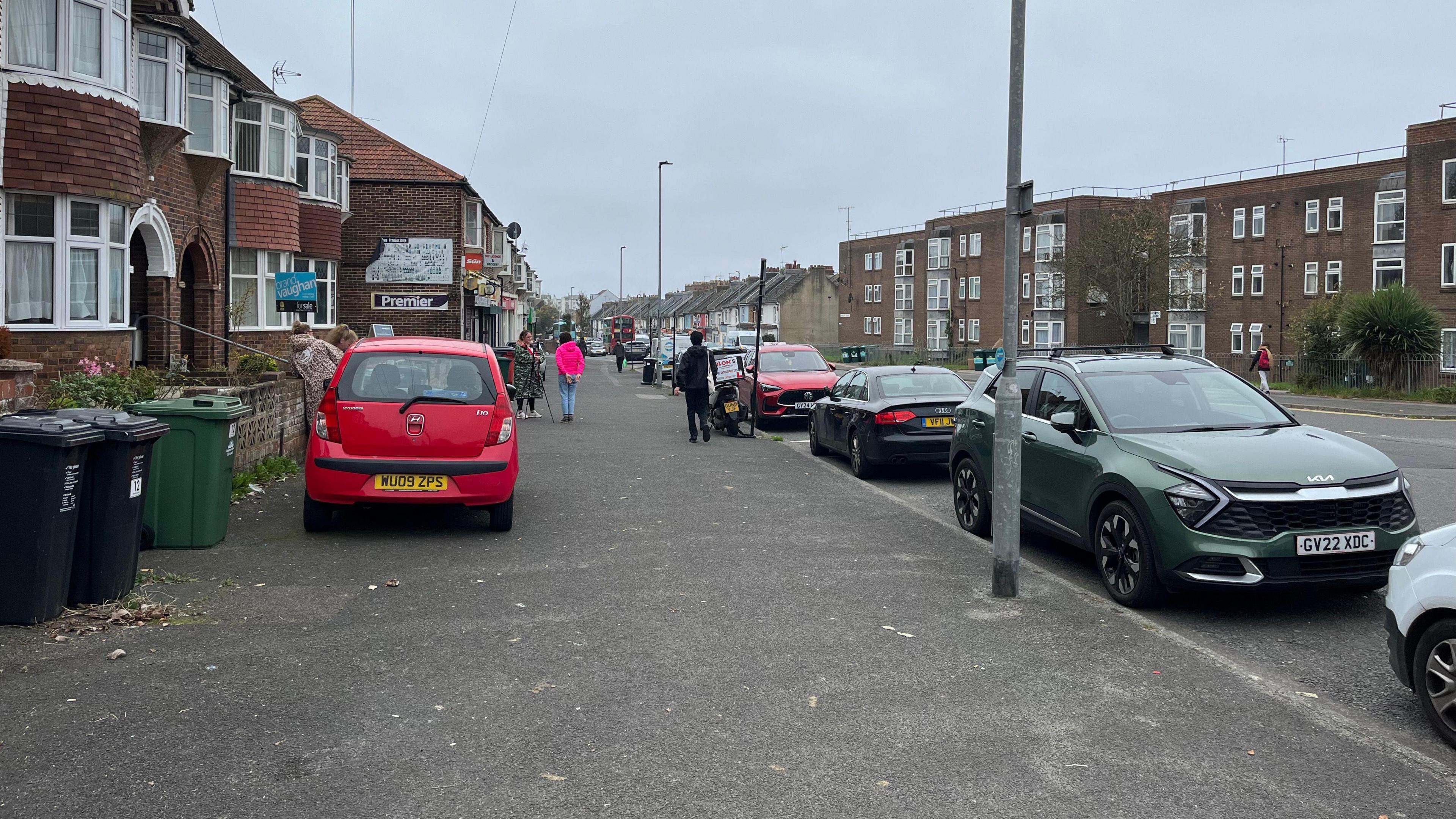 Whitehawk Road with shops on one side and flats on the other. The pavement is about 15ft wide.